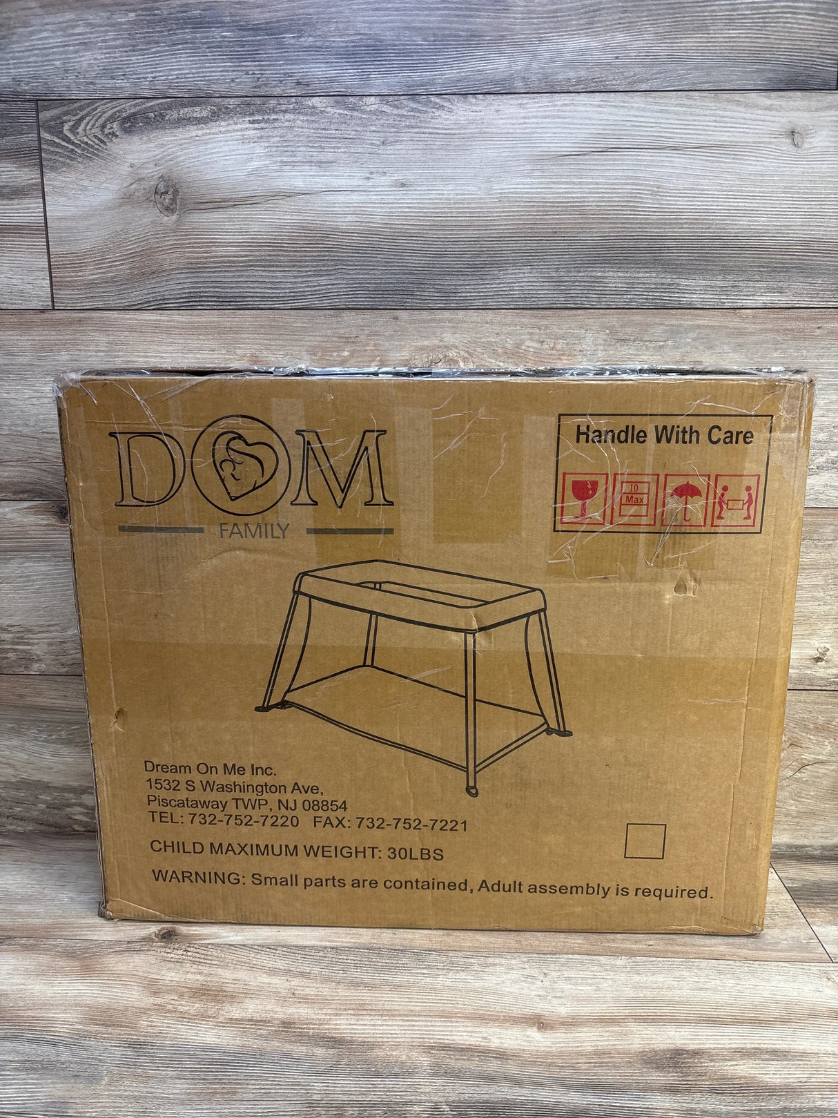 Front of boxed Dream On Me Travel Light playard with printed drawing, brand logo and Handle With Care label on wood floor