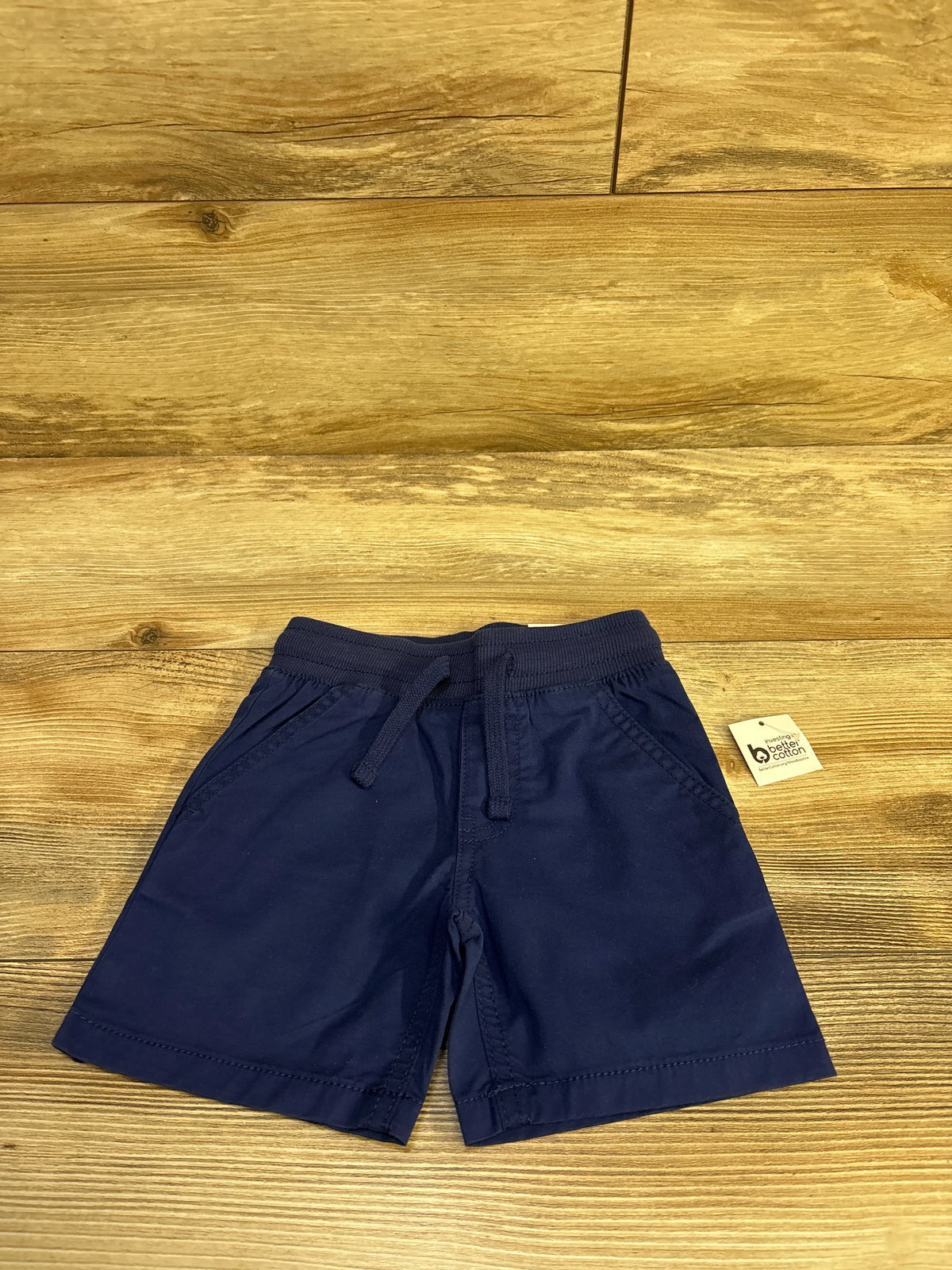 Front view of Epic Threads navy pull-on toddler shorts showing elastic waistband with drawstring and side pockets on wood floor background