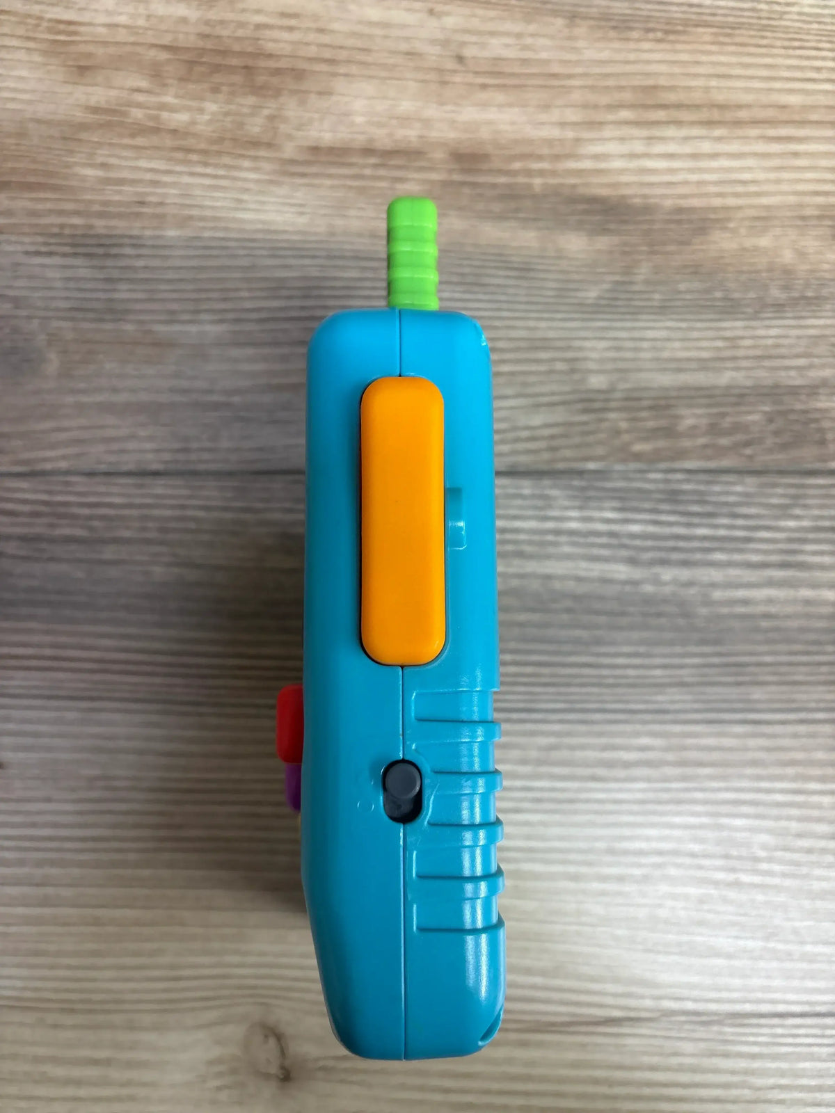 Front view of Fisher-Price Laugh & Learn Lil’ Gamer handheld toy showing blue and orange plastic body and buttons on a wood surface