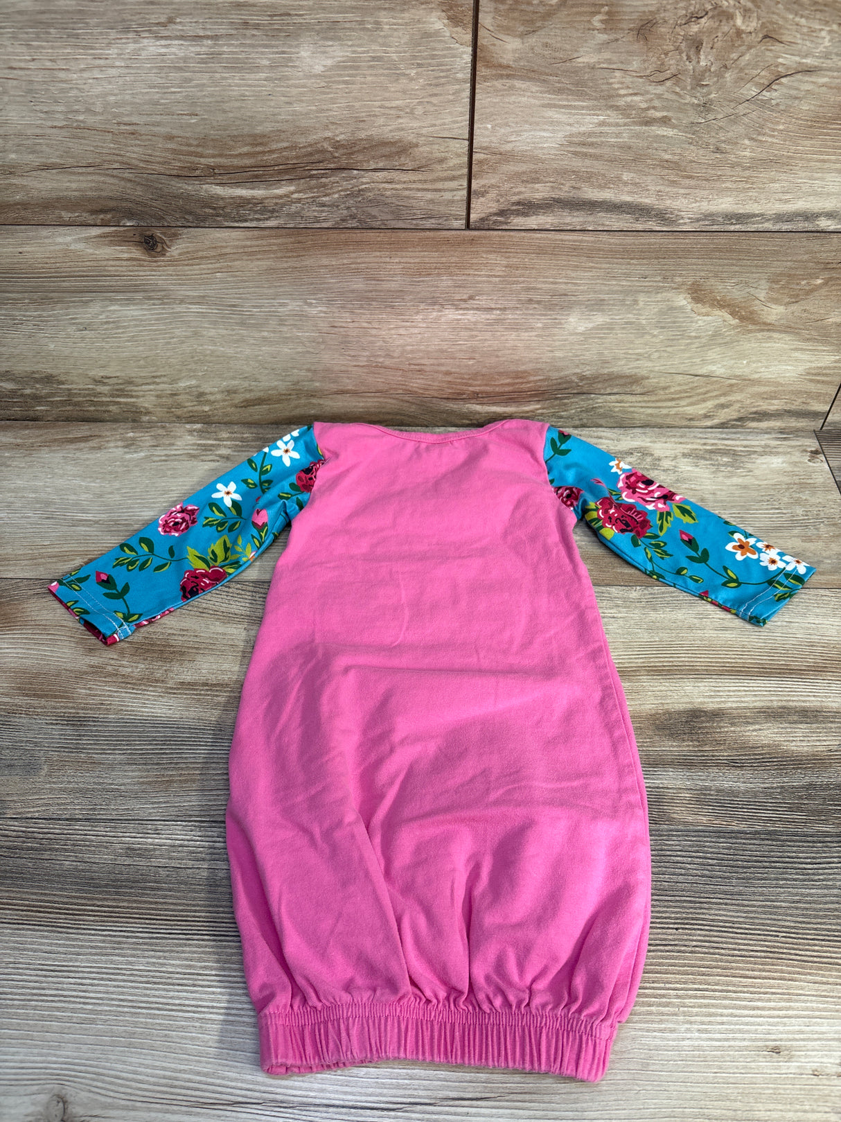 Pink baby gown with blue floral long sleeves on wooden background