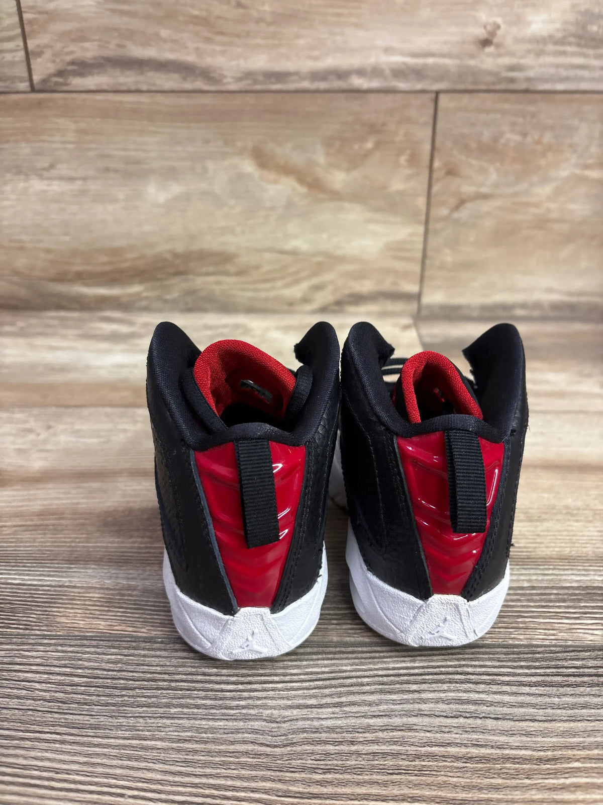 Rear view of Air Jordan B’Loyal PS White Gym Red sneakers showcasing black uppers, red heel panels, and white midsoles on wood flooring