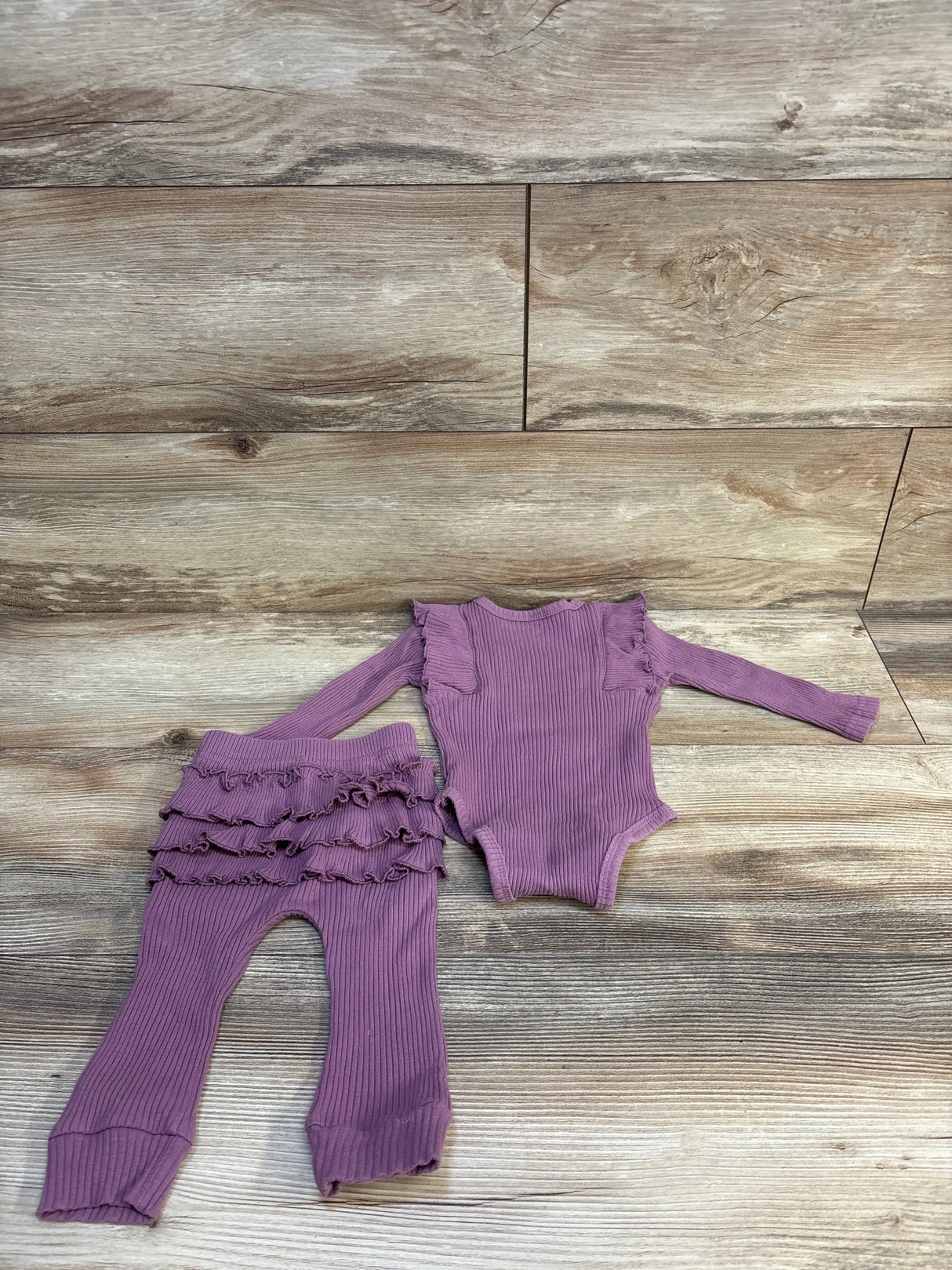 Purple ribbed baby onesie and ruffle leggings set on wood floor