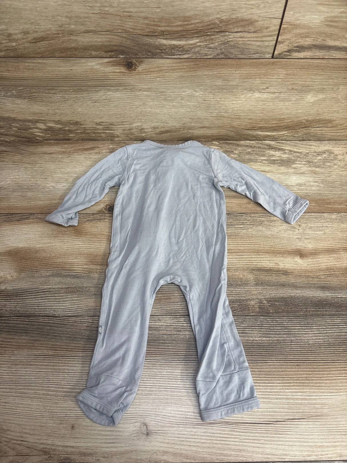 Light gray long-sleeve baby onesie laid flat on wood floor background