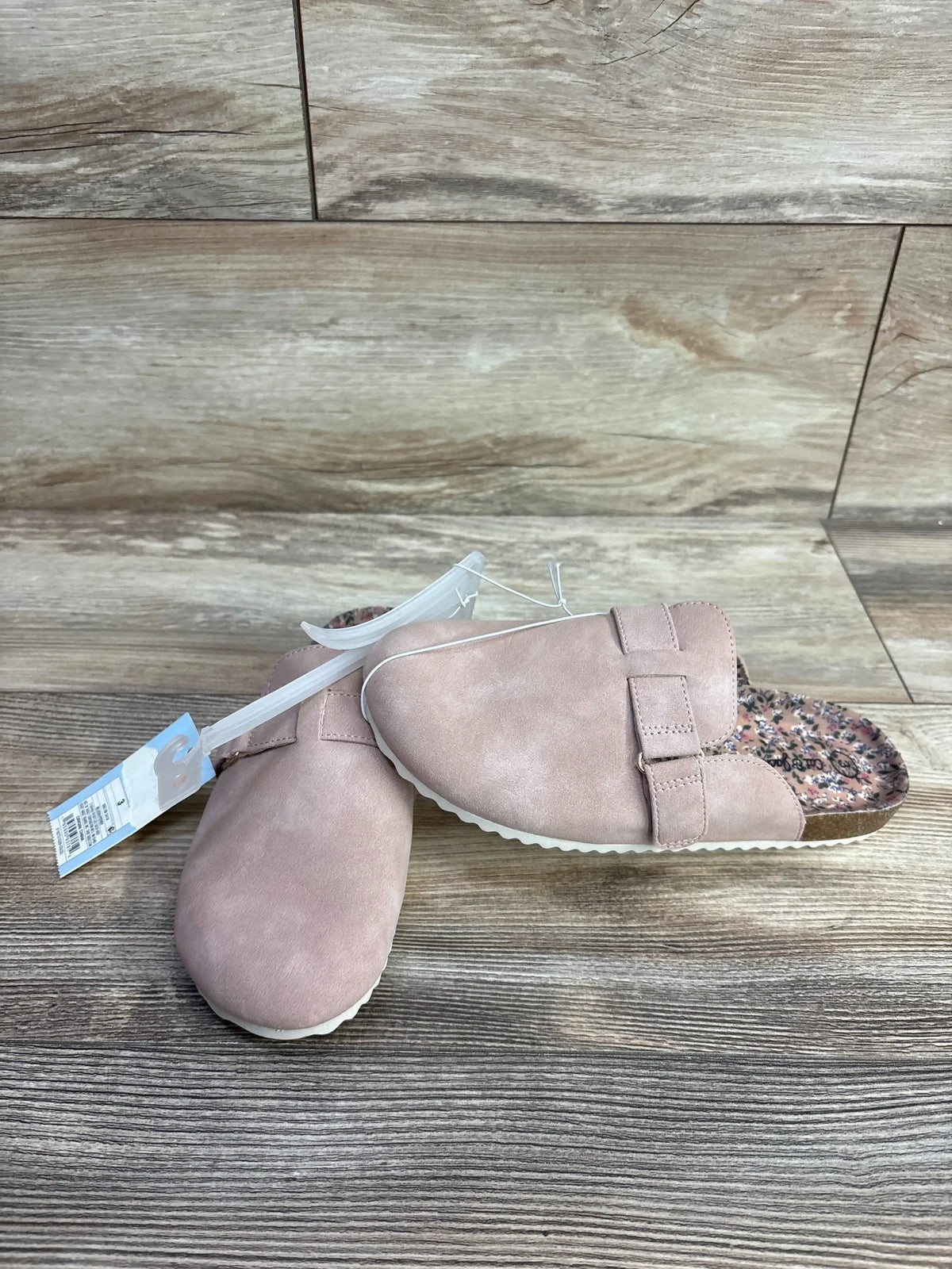 Pair of pink children's slip-on shoes with adjustable straps and floral inner lining on wood floor