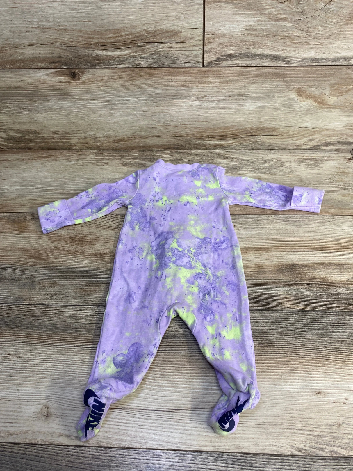 Purple and yellow tie-dye baby sleeper with footies featuring navy Nike logo on hardwood floor