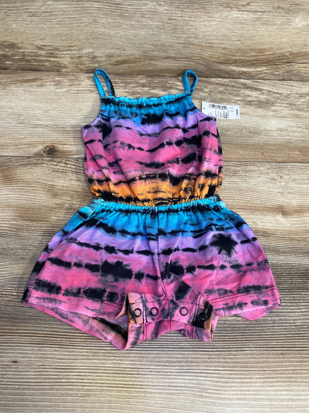 Top-down view of Children's Place tie-dye baby romper with elastic waist, spaghetti straps and snap crotch on wood background