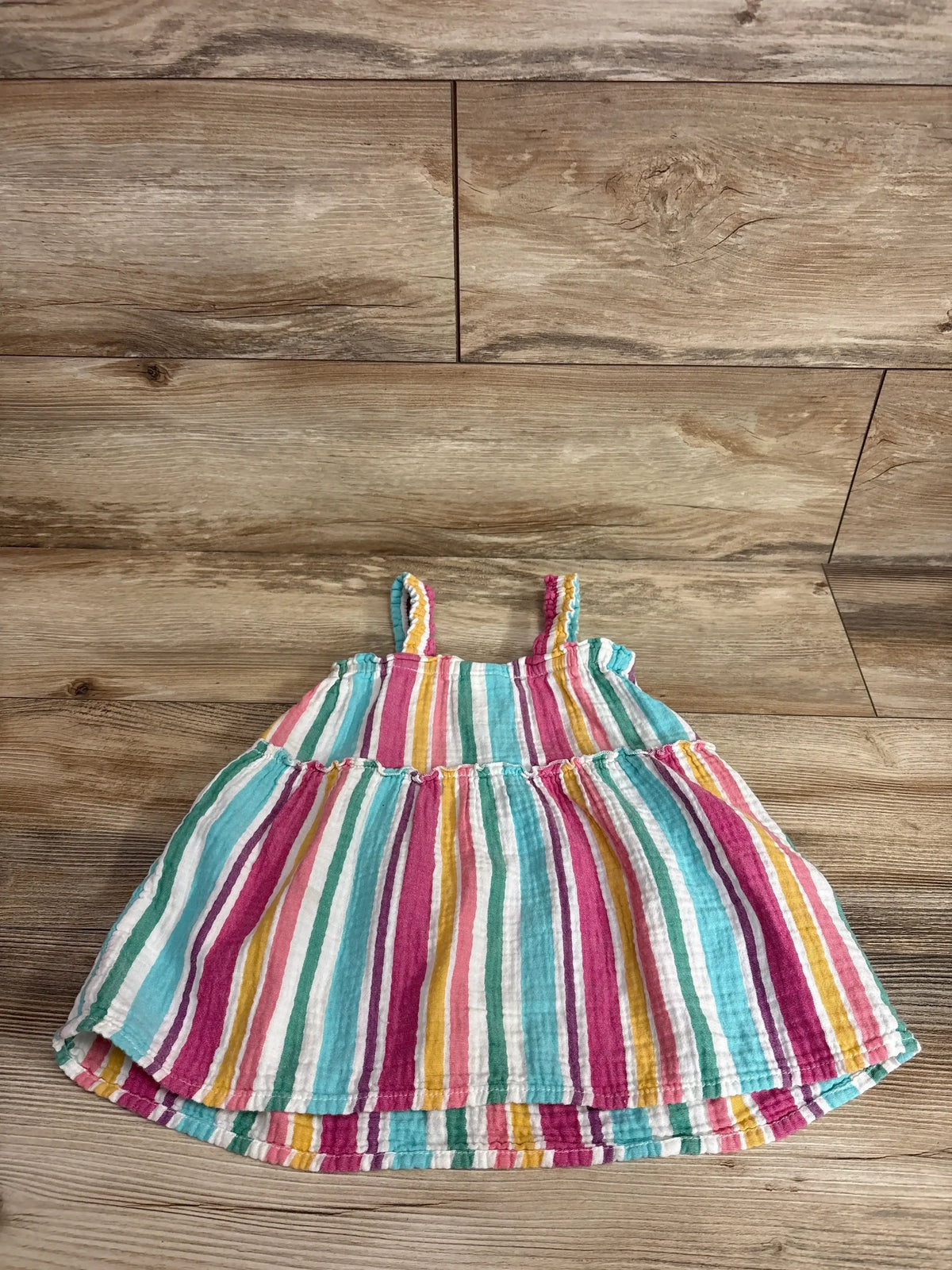 Front view of Cat & Jack 100% cotton muslin tank dress, size 2T, with colorful stripes and thin straps on wood-look floor