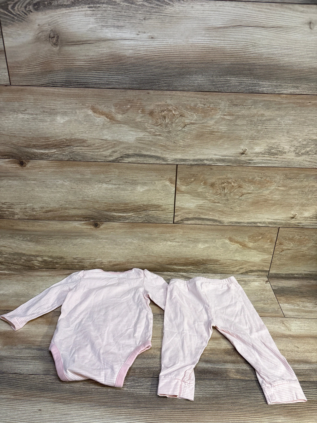 Flat-lay of Baby Gap 2-piece pink striped bodysuit and pants set showcasing long sleeves and elastic waist with wood floor background