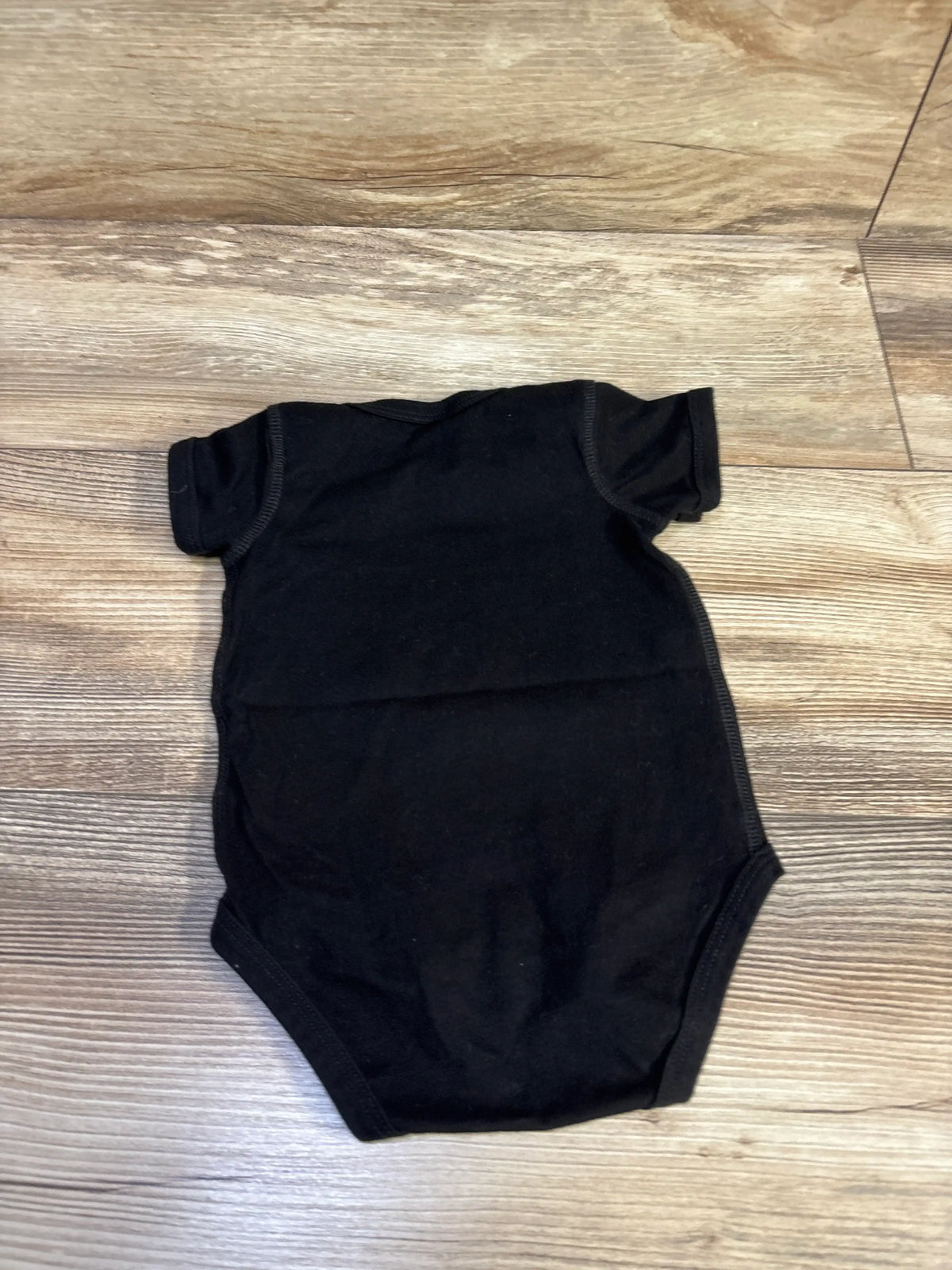 Flat lay of a black Rabbit Skins baby bodysuit in size 12 months with short sleeves on a wood-look floor