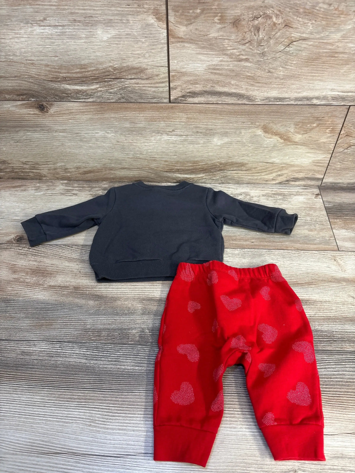 Top-down view of Cat and Jack newborn 2-piece sweatshirt set showing the back of the grey long-sleeve sweatshirt and red heart-print pants on a wood floor
