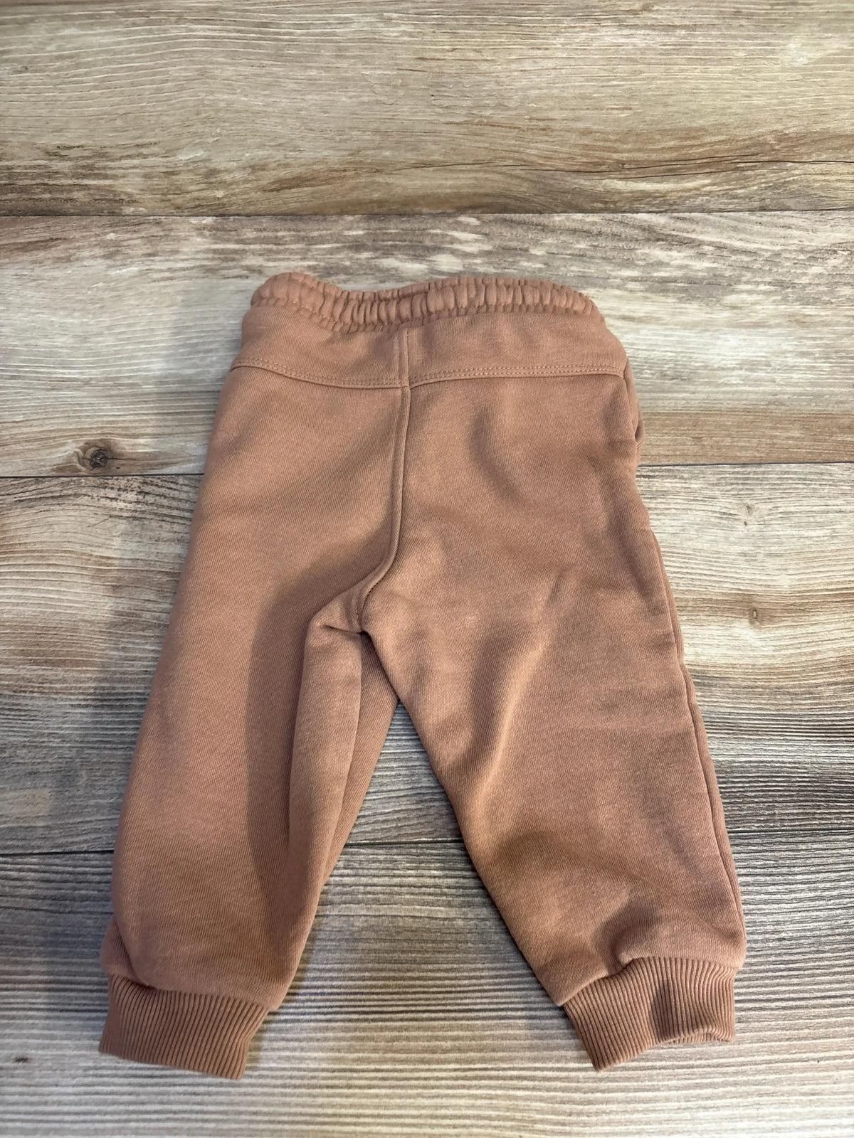 Soft brown kids joggers with elastic waist and cuffs, laid on wood floor