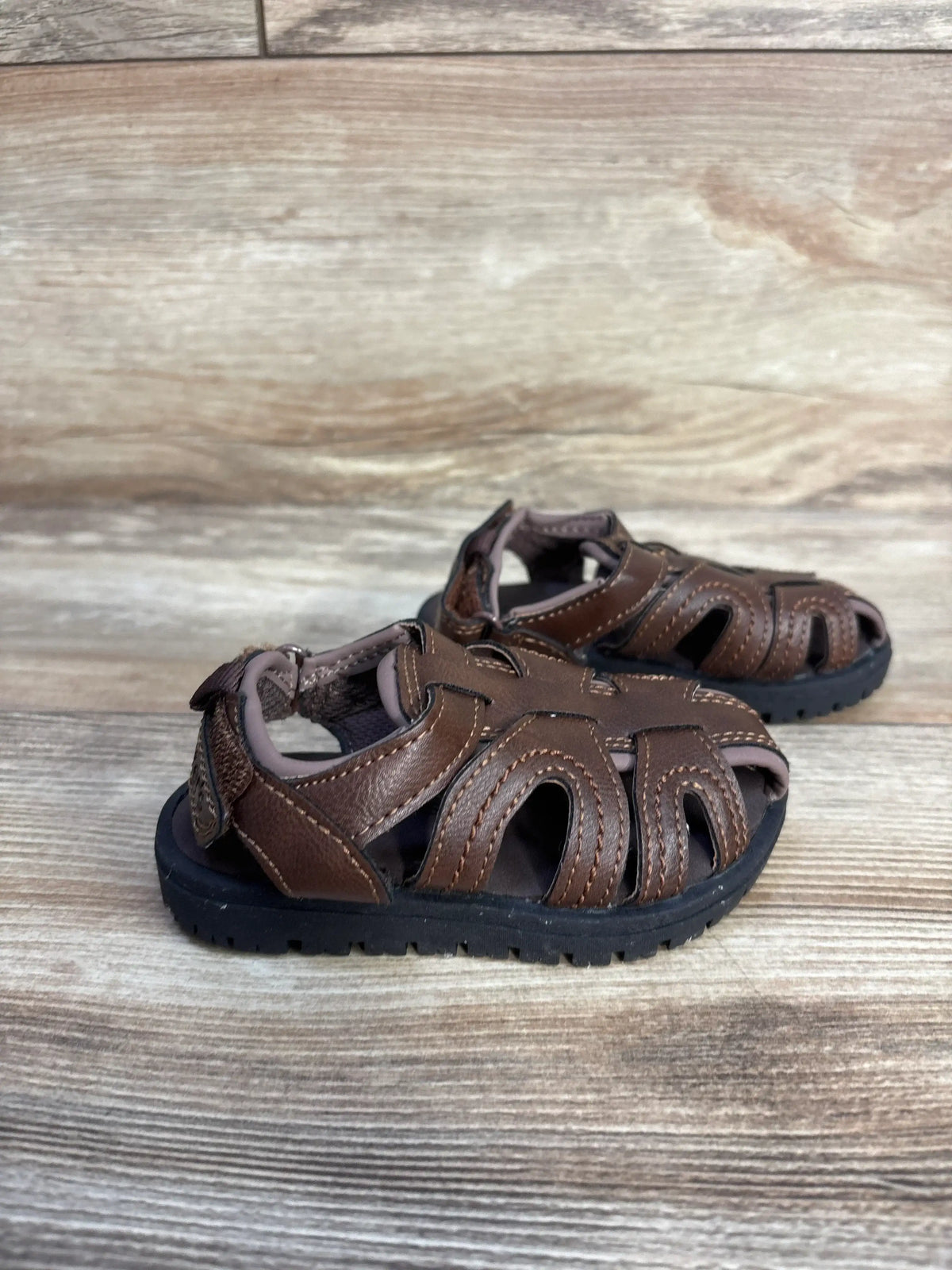 Three-quarter view of Carter’s Vasco brown sandals showing straps and deep-groove soles on wood flooring