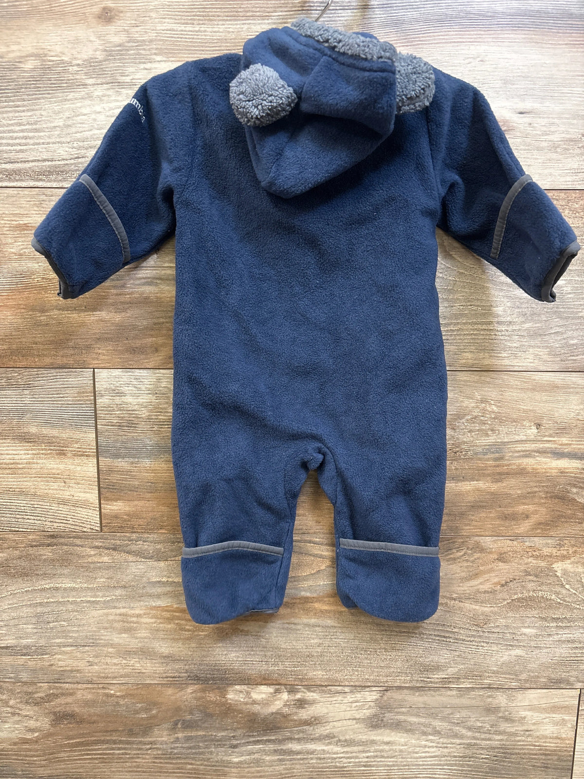 Back view of Columbia Tiny Bear II Bunting in navy, size 3-6 months, showcasing bear-ear hood and gray trim on a wood floor
