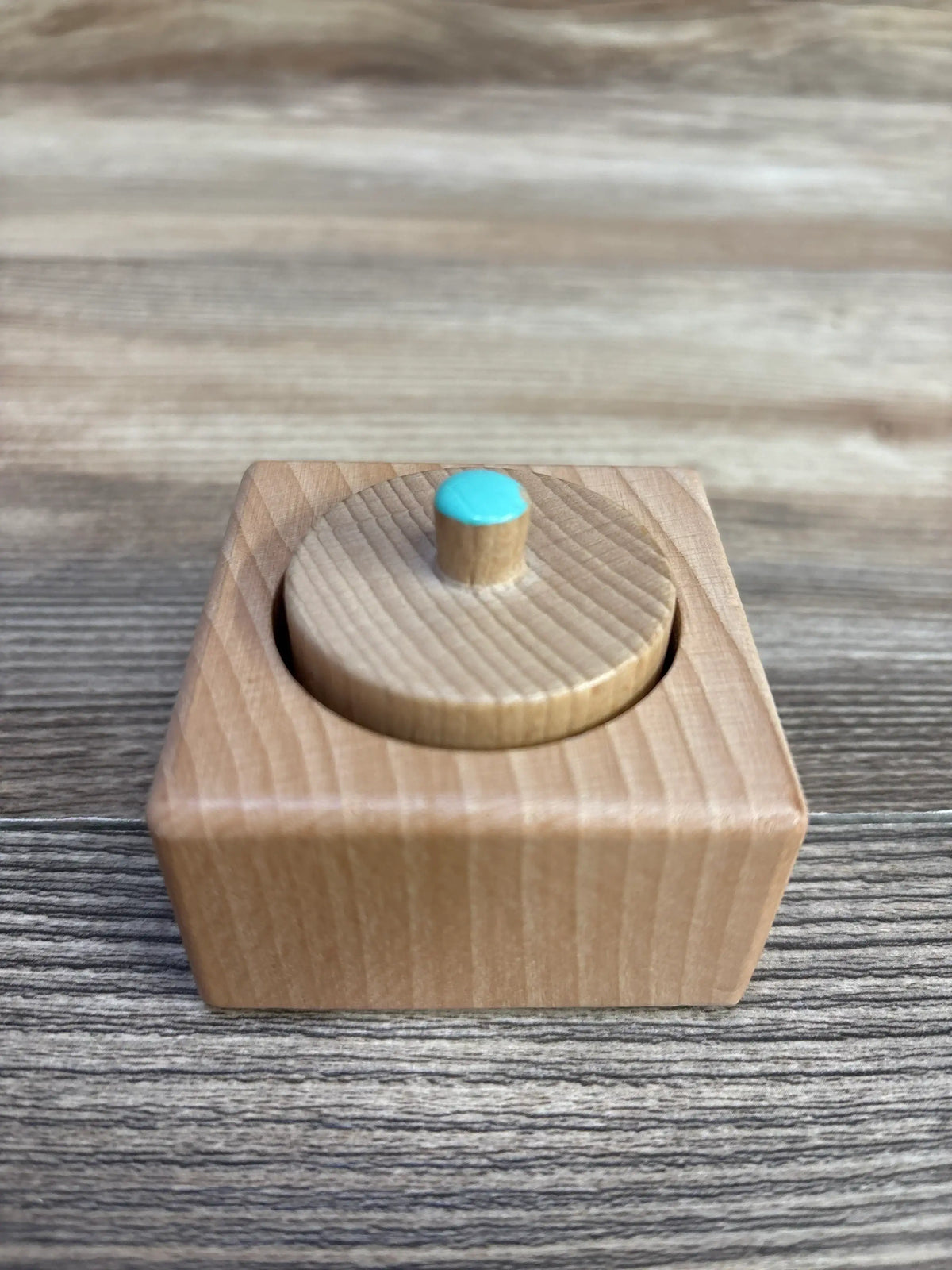 Top-down view of Lovevery Pincer Puzzle wooden knobbed cylinder with blue top on wood-grain background