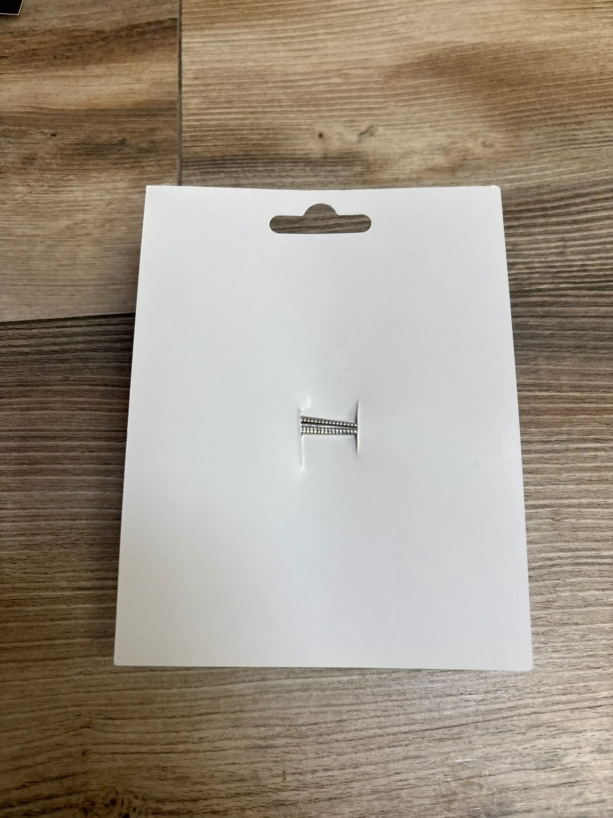 Silver ring with small gemstones on white jewelry card, displayed on wood background