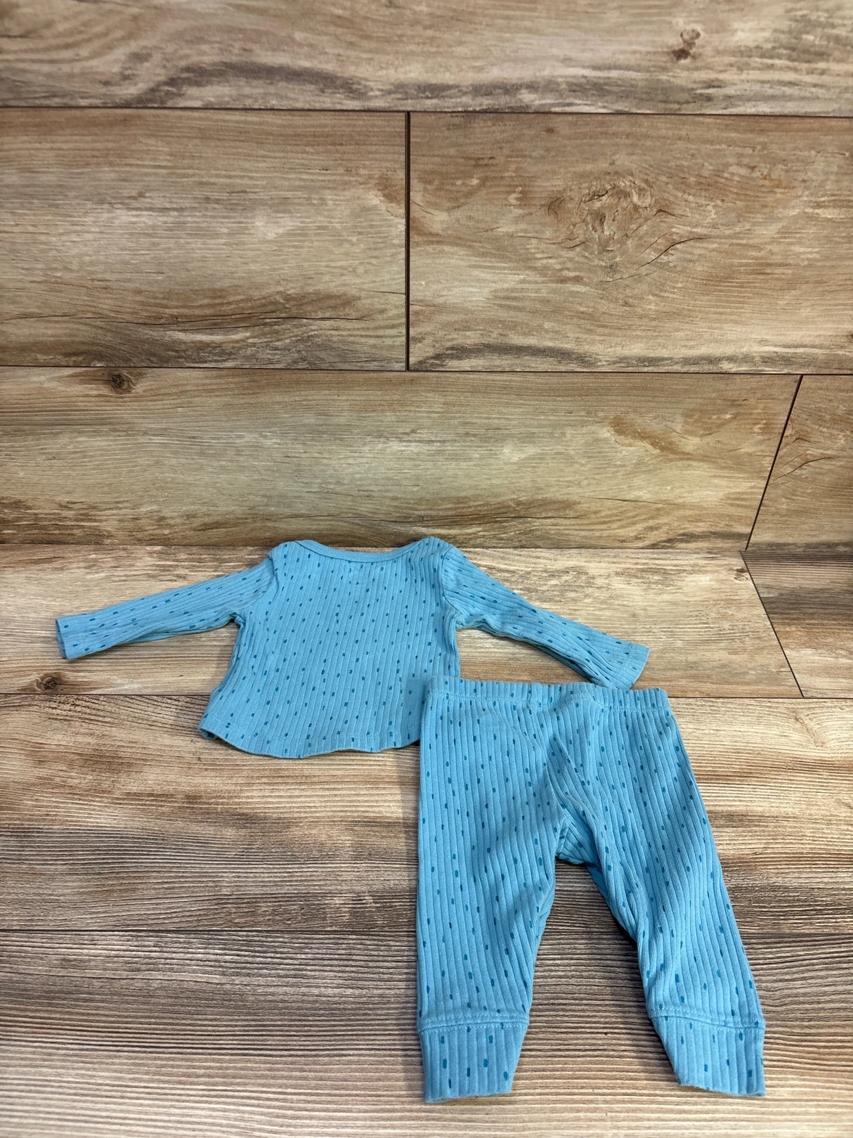 Flat lay of 2-piece ribbed baby shirt and pants set in blue showing ribbed texture and small dots on wood background