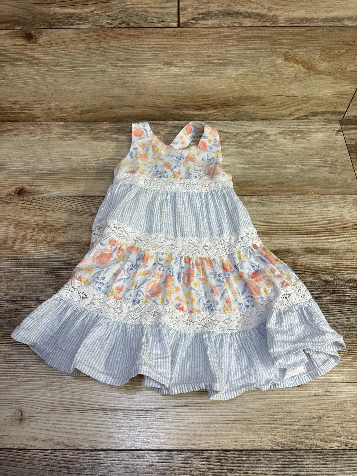 Front view of Tommy Bahama sleeveless tiered dress showcasing floral panels, blue striped tiers, and lace trim on a wood floor