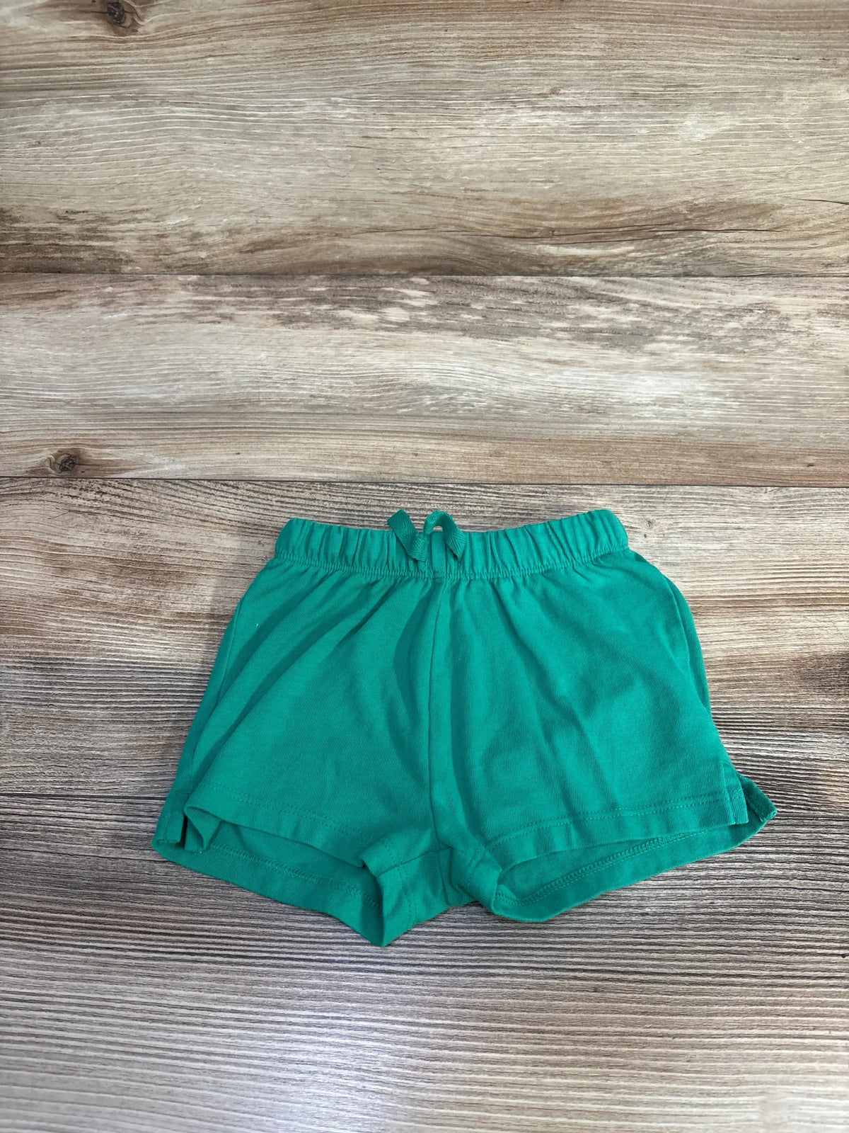 Flat lay of green Cat & Jack toddler drawstring shorts size 12 months showing elastic waistband and front tie on wood background