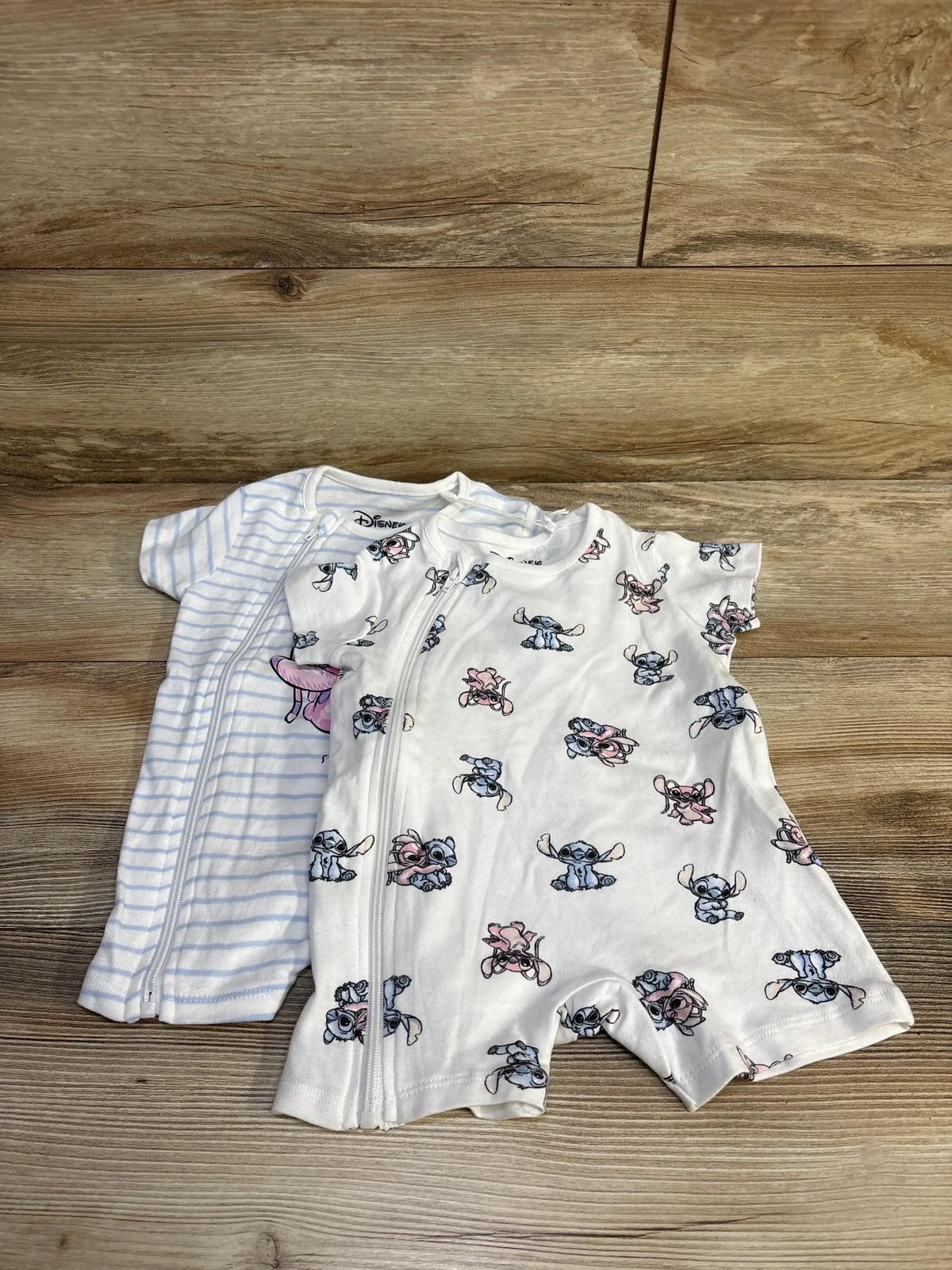 Front view of Sinsay Disney Baby Lilo and Stitch two shortie rompers with striped and character prints on wood flooring