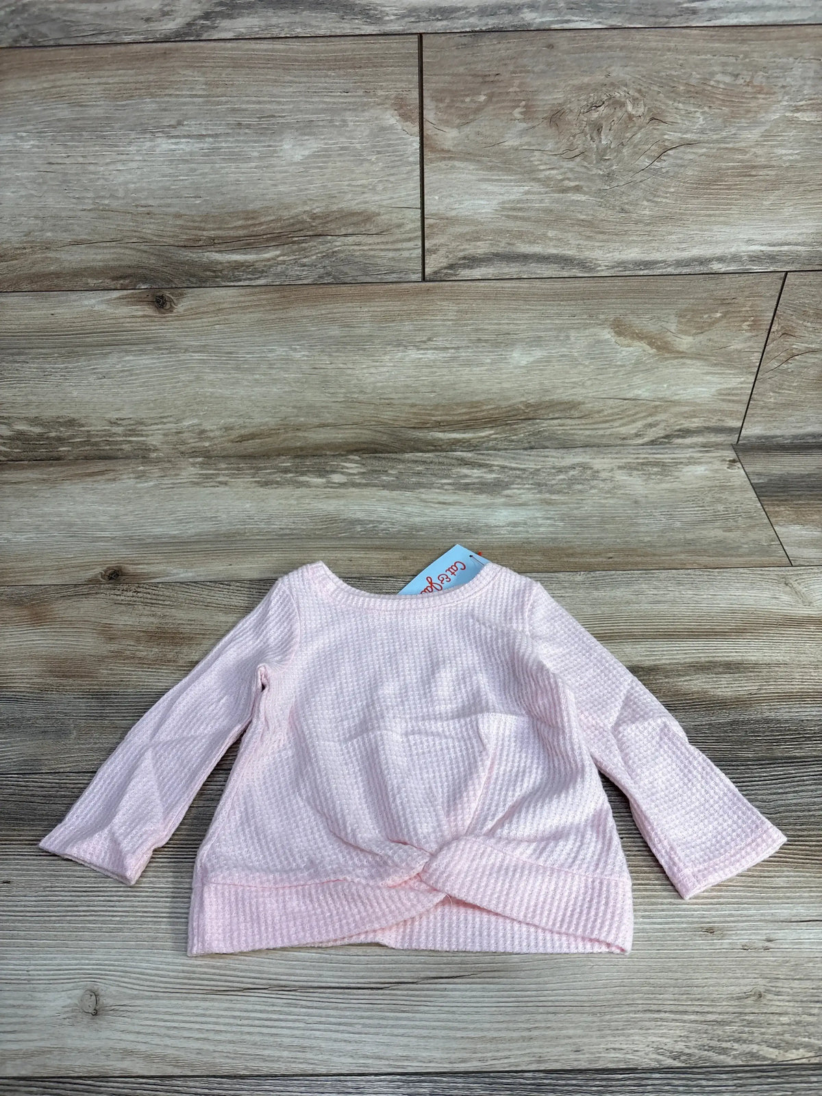 Light pink waffle knit toddler long sleeve shirt with a front knot, on wood background