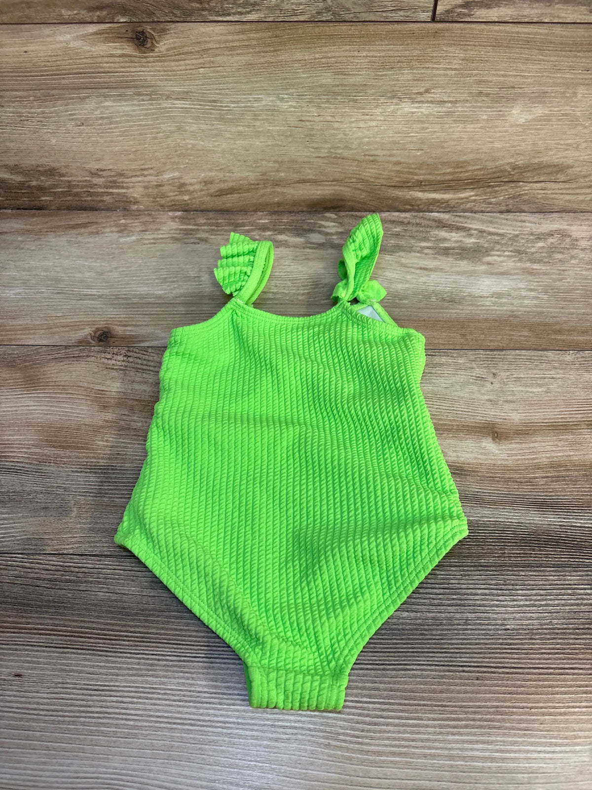 Top view of green Shein cut-out swimsuit showcasing textured fabric and tie shoulder straps on a wood background