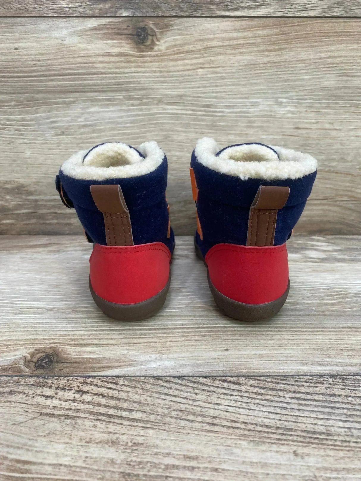 Rear view of Double B. miki House baby boots showing navy and red colors, fleece lining, pull tabs on wood background