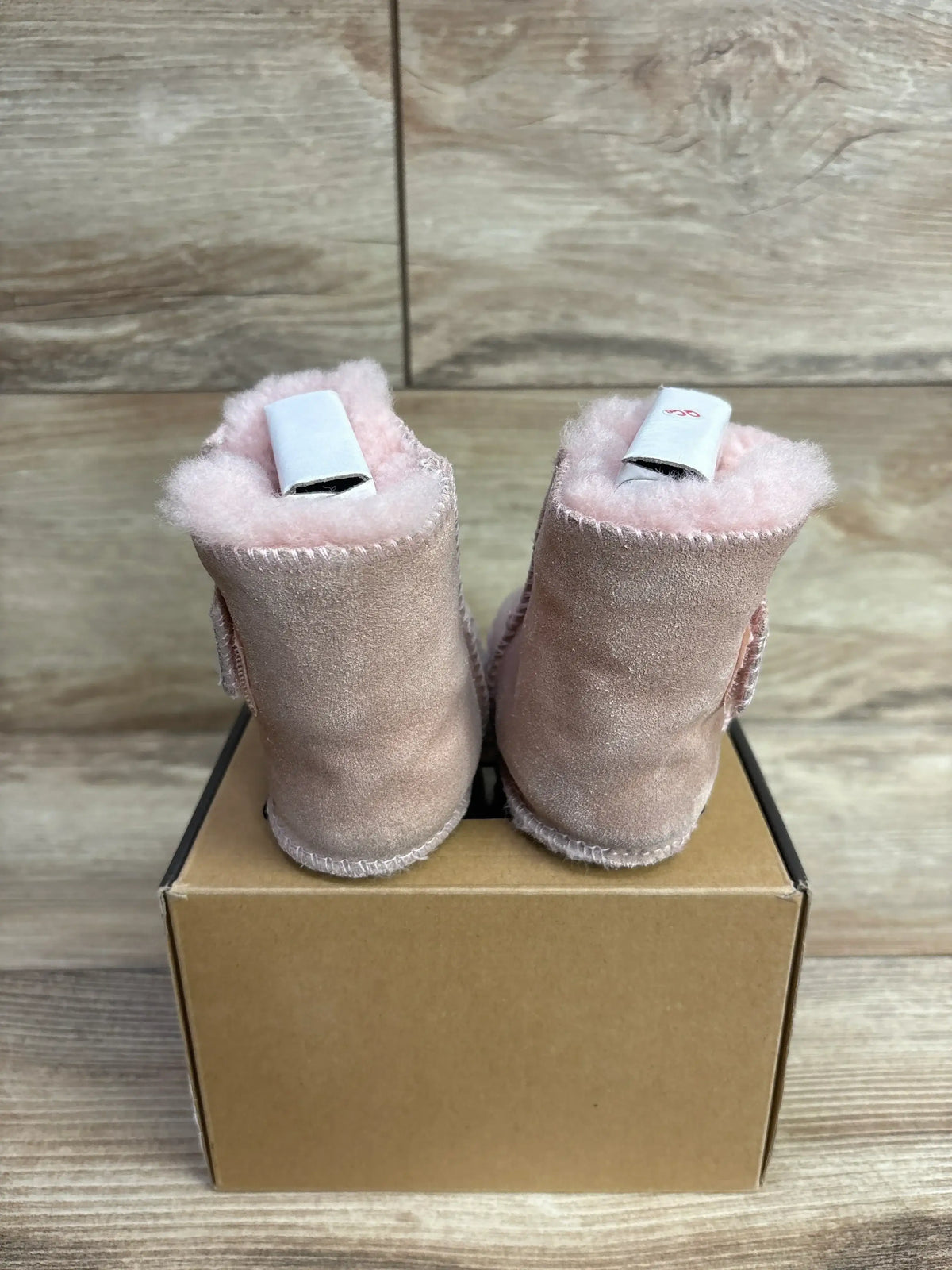 Rear view of UGG Erin baby booties in soft pink showing plush shearling lining on a cardboard box over wooden surface