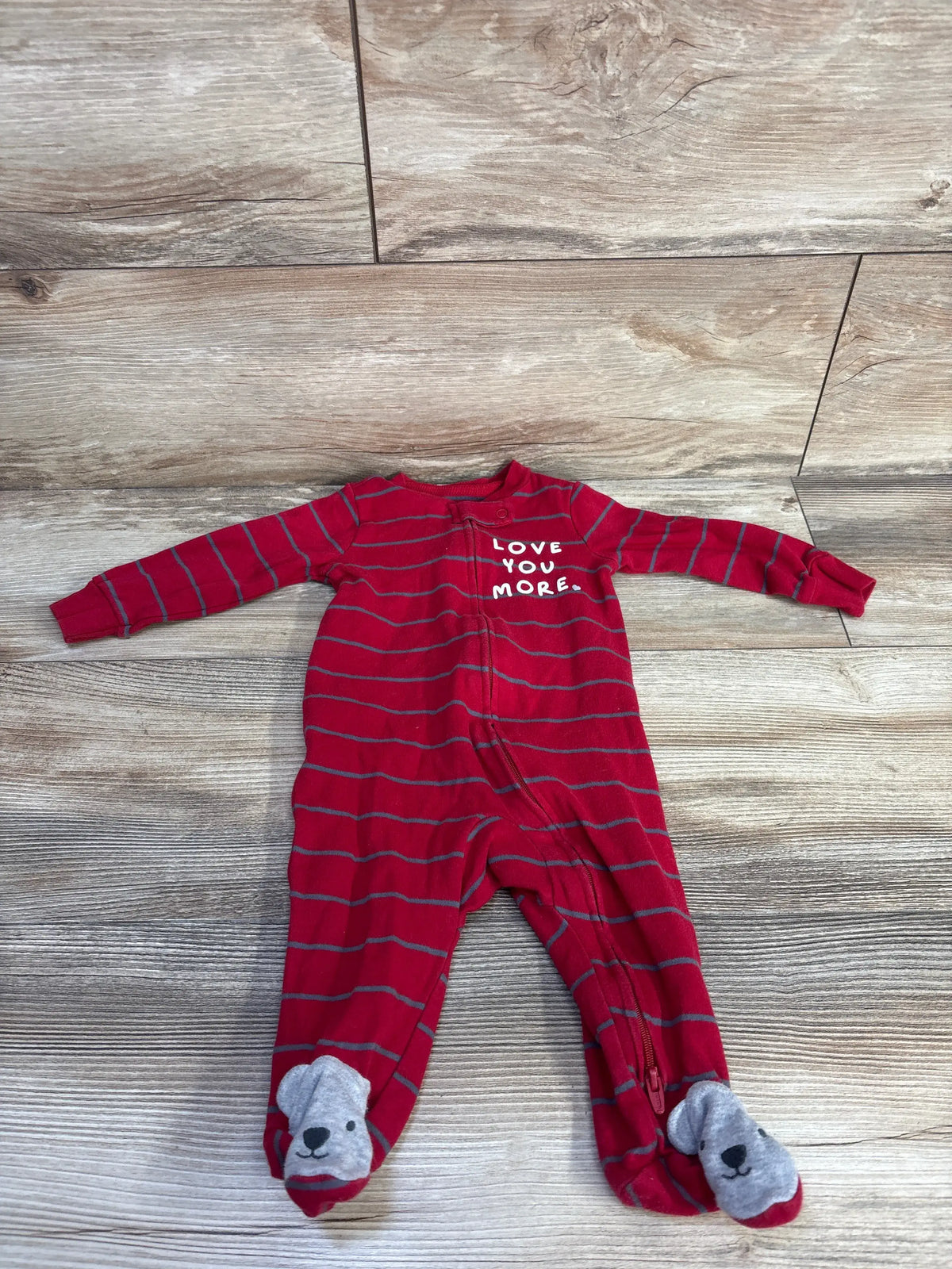 Front view of red striped Just One You sleeper showcasing Love You More text and gray bear face footies on a wood floor