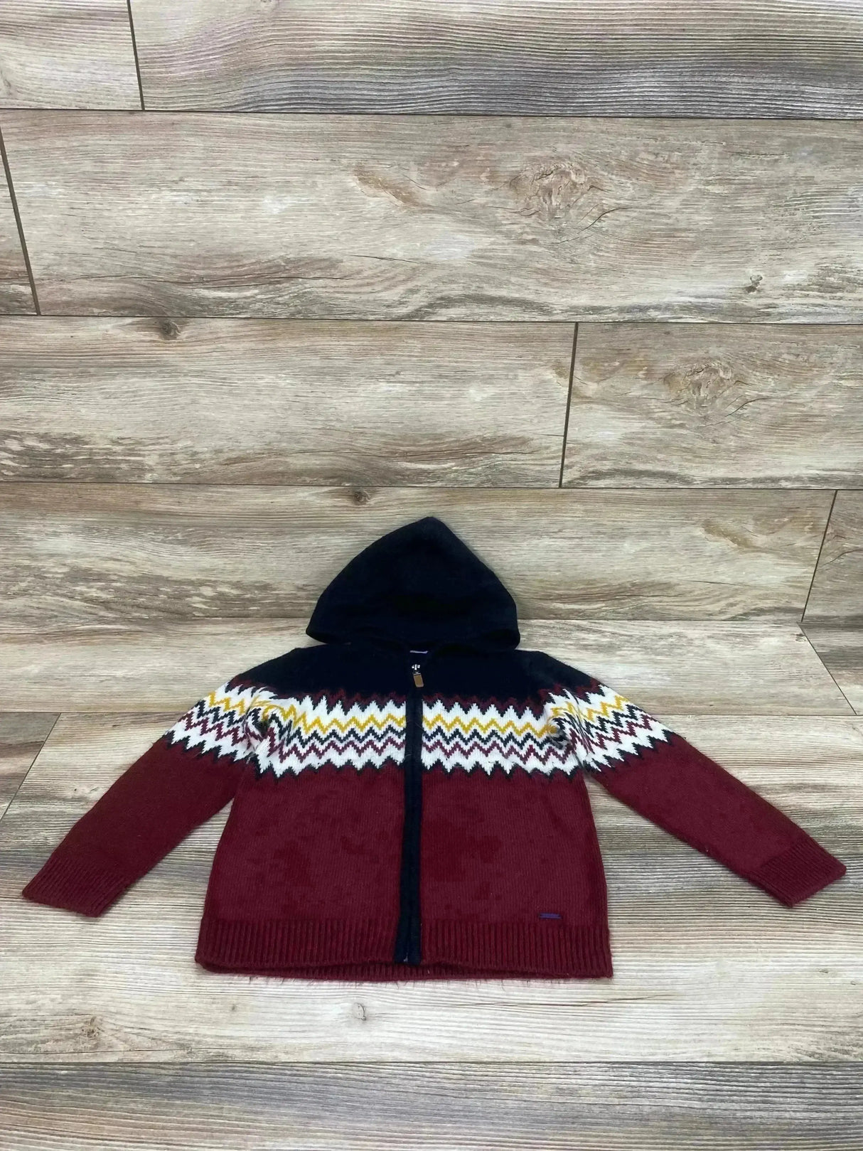 Flat lay of Mayoral full-zip knit hoodie, navy and burgundy, showing zigzag yoke, hood, and zipper on light wood background