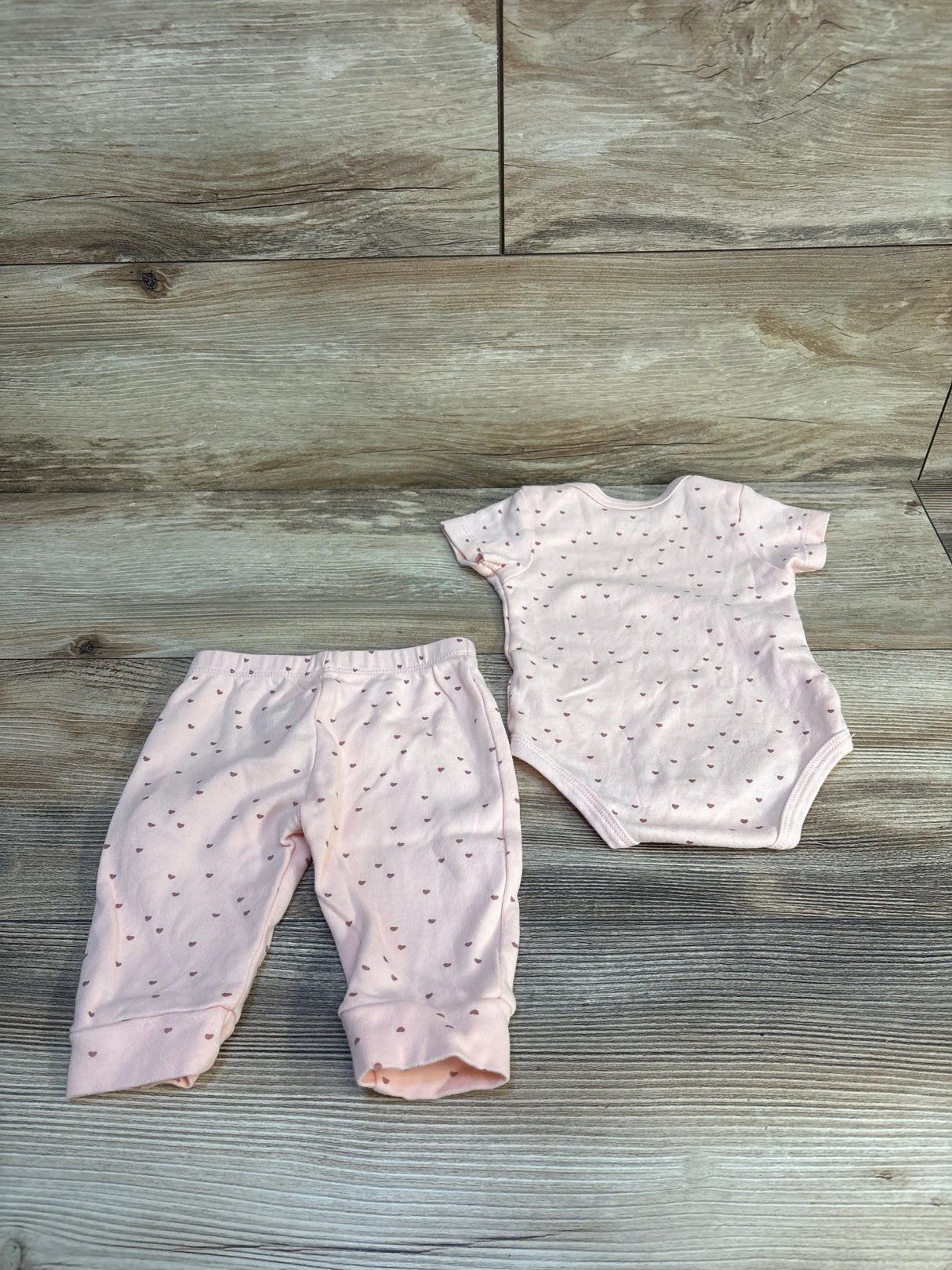 Pink baby onesie and pants set with heart print, soft newborn clothing on wood floor
