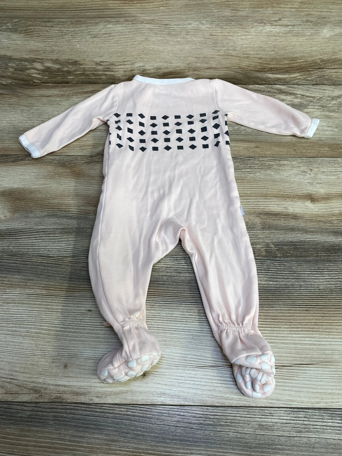 Back view of pink Nanit Breathing Wear footed pajamas showing black back breathing panel and white non-slip sole grips on wood