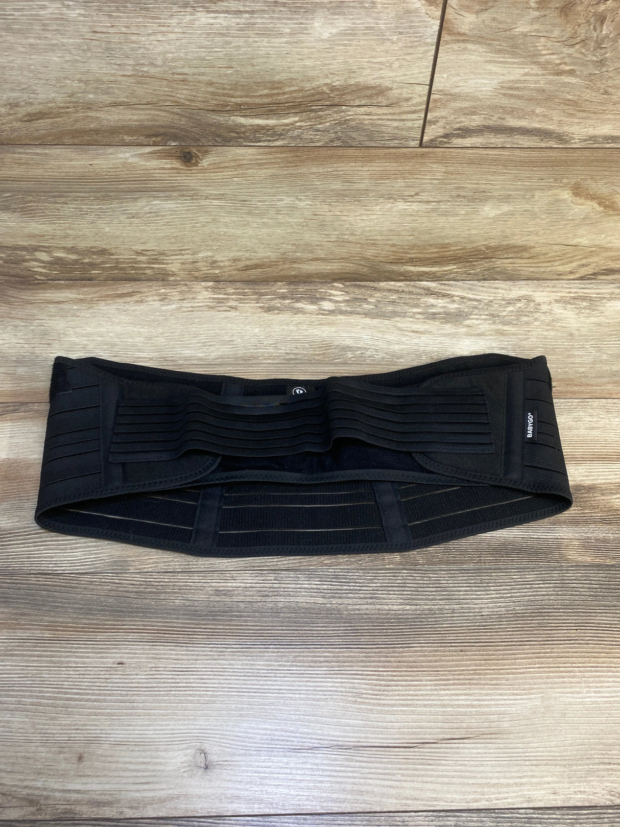 Black adjustable maternity or postpartum support belt on wooden floor