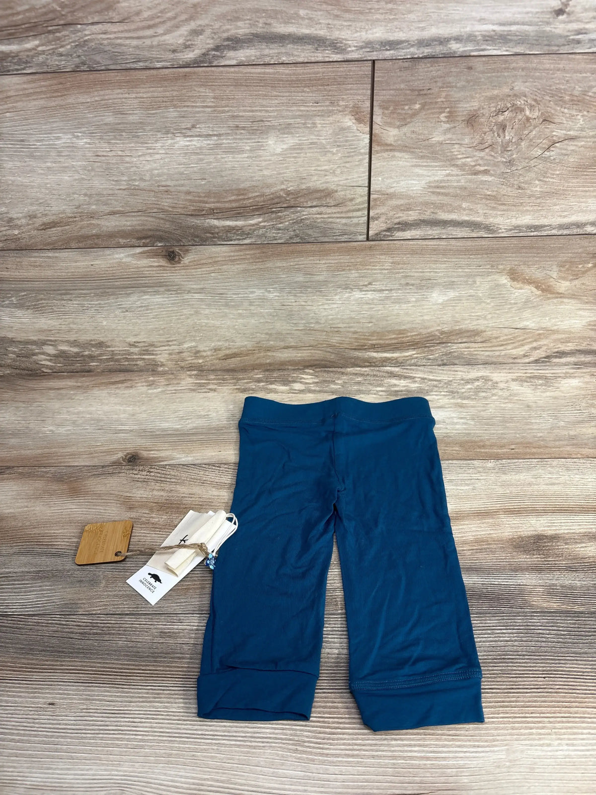 Top view of Kickee Kids peacock pants 3-6M showing elastic waist and cuffed legs on wood floor, new with tags