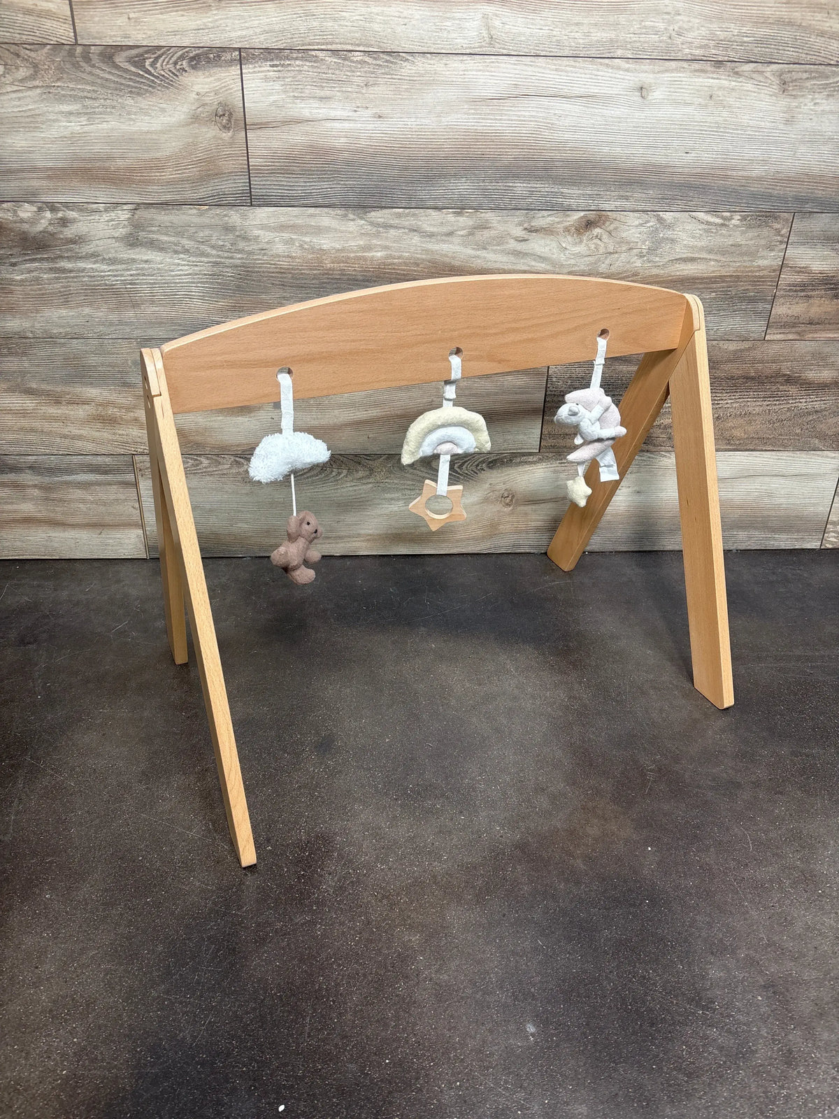 Front view of Pottery Barn Kids wooden activity gym showcasing three hanging cotton fleece toys on a wood floor
