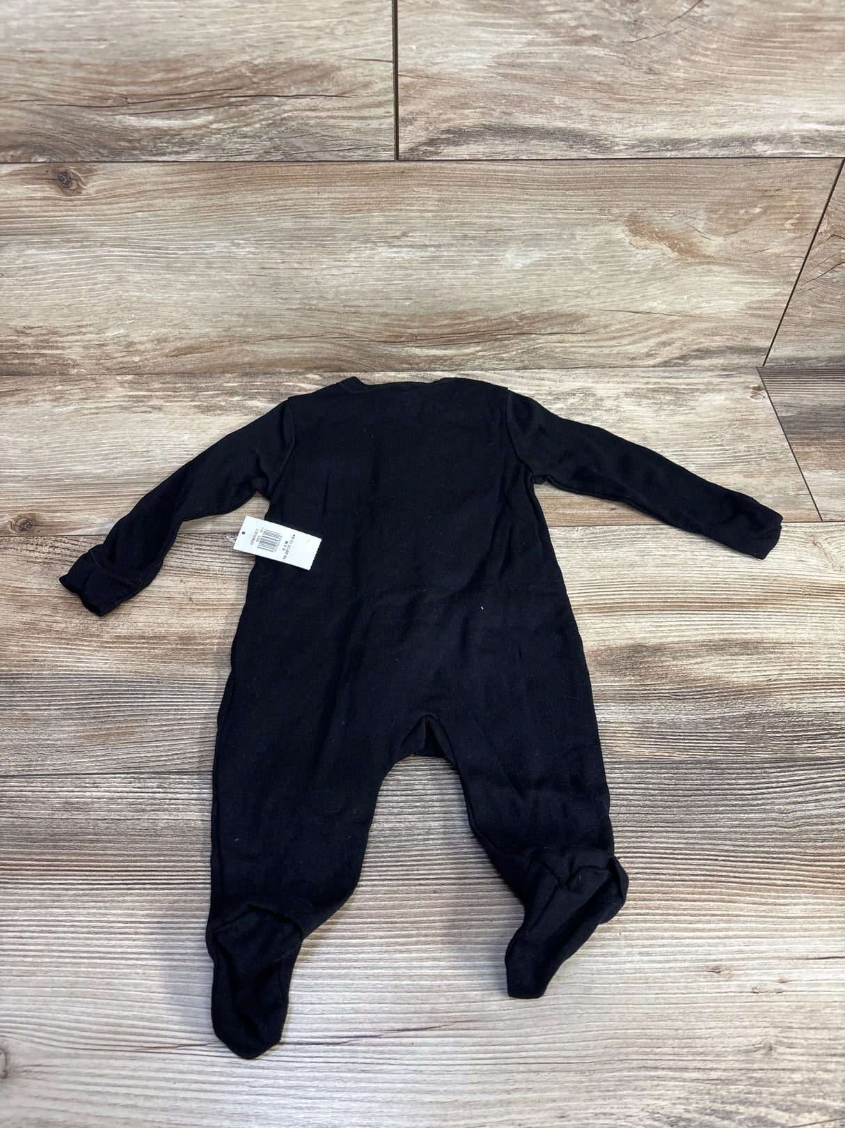 Black baby footed onesie with tag, laid flat on wood floor for resale