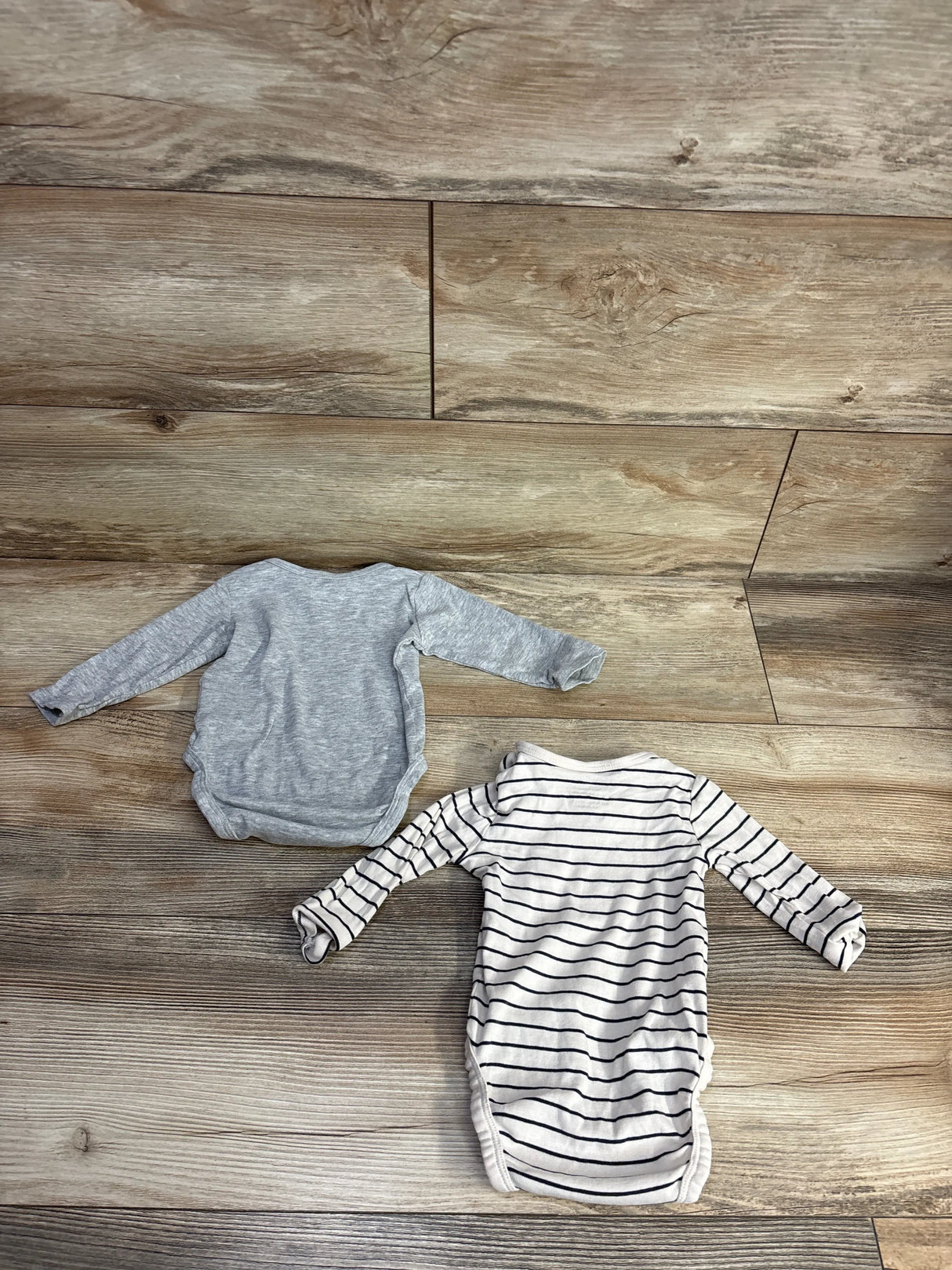 Two long sleeve baby bodysuits, one gray and one striped, on wood floor
