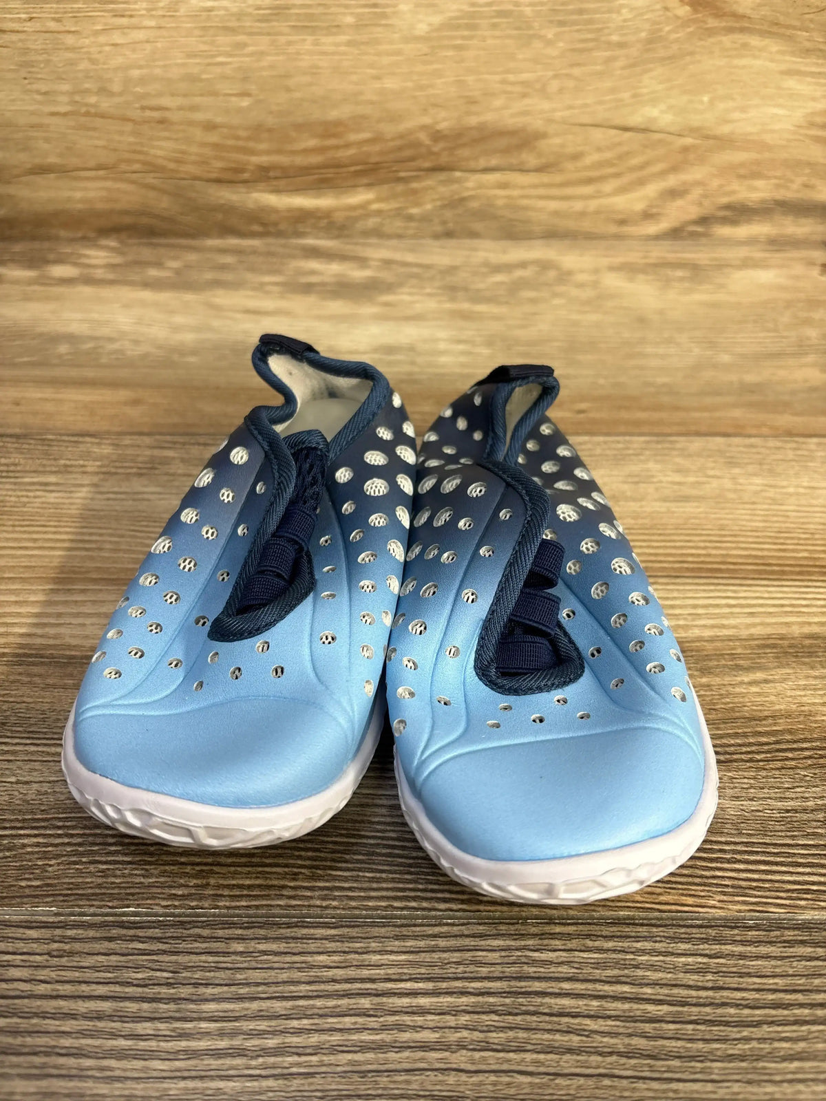 Front view of Fires Barefoot quick-dry water shoes, light blue, perforated upper, navy elastic laces, white sole on wood