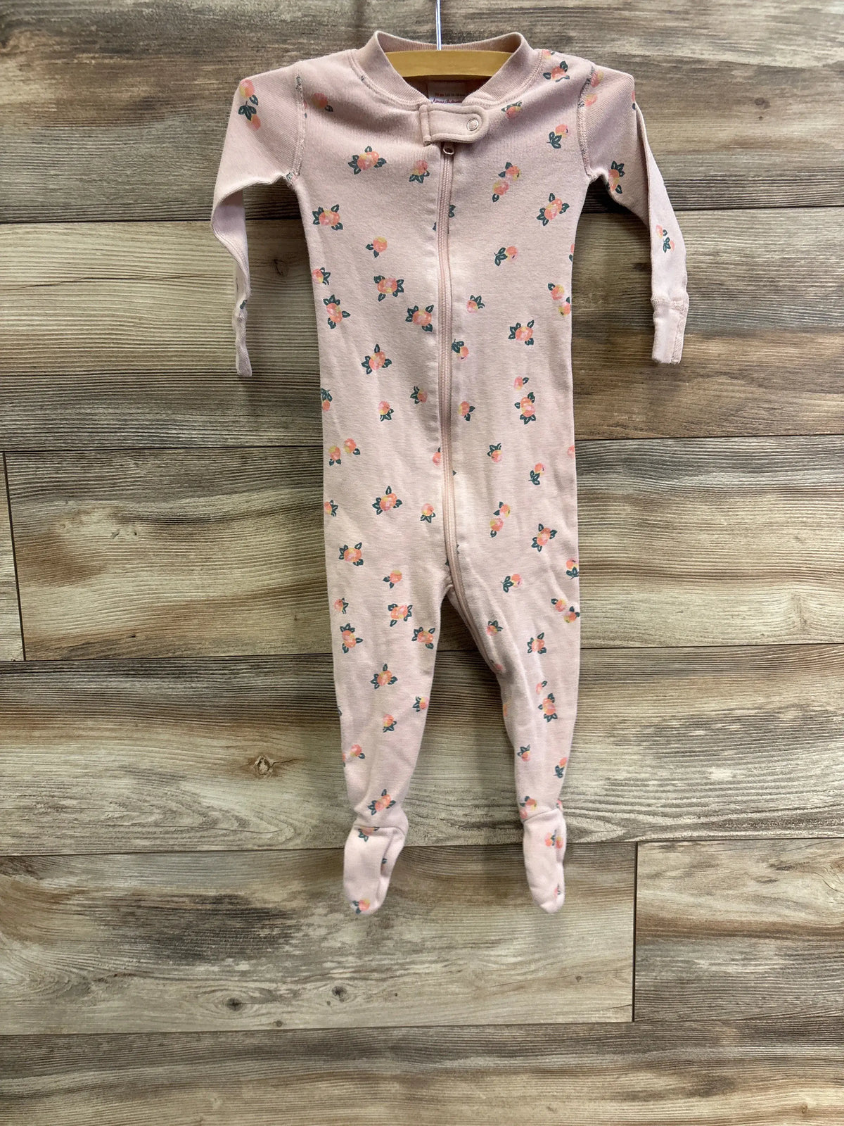 Front view of Hanna Andersson pink floral sleeper showcasing footed legs and full-length zipper on wood background