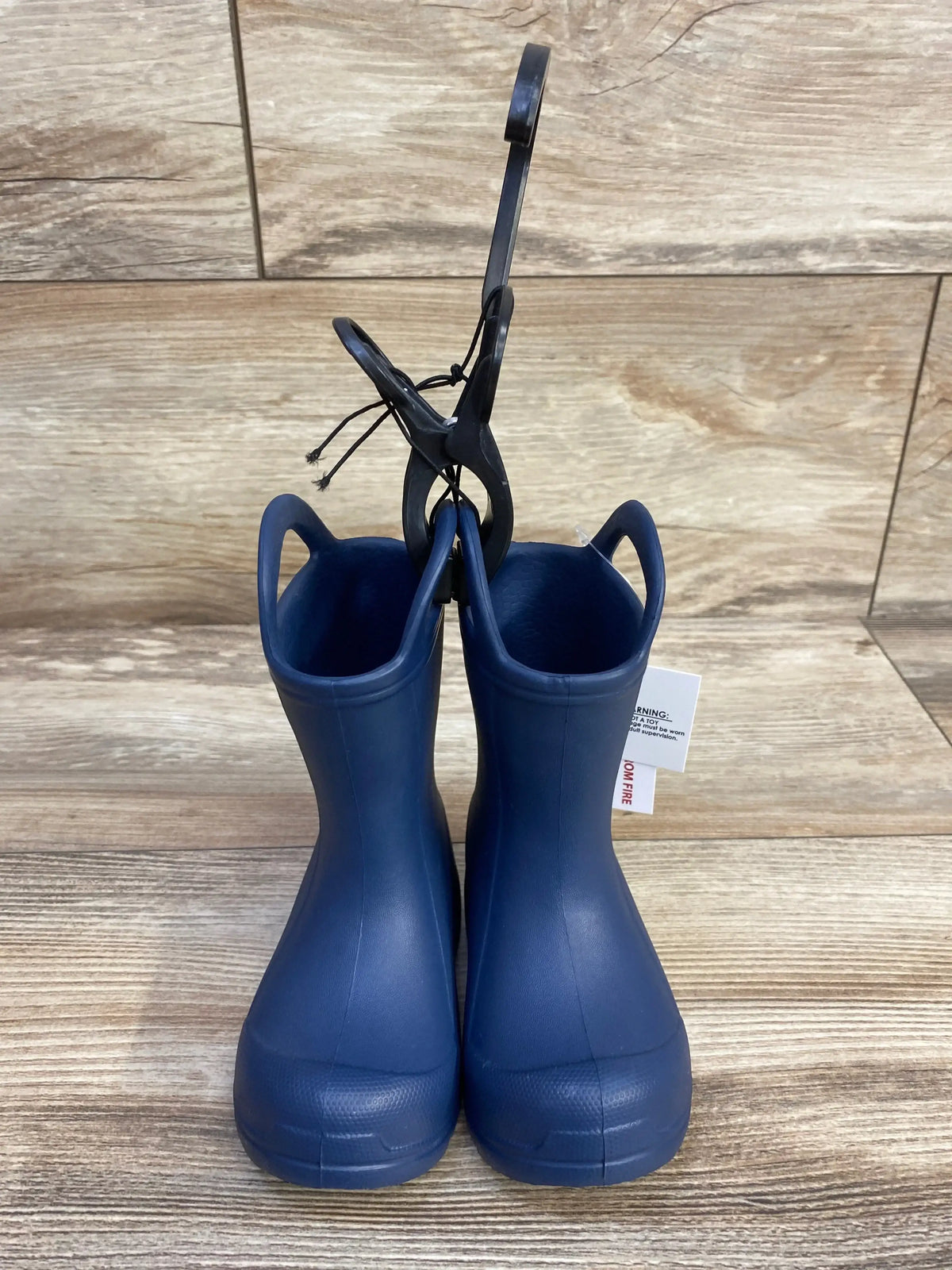 Front view of navy BEARPAW EVA toddler rain boots with easy pull-on handles on wood plank background