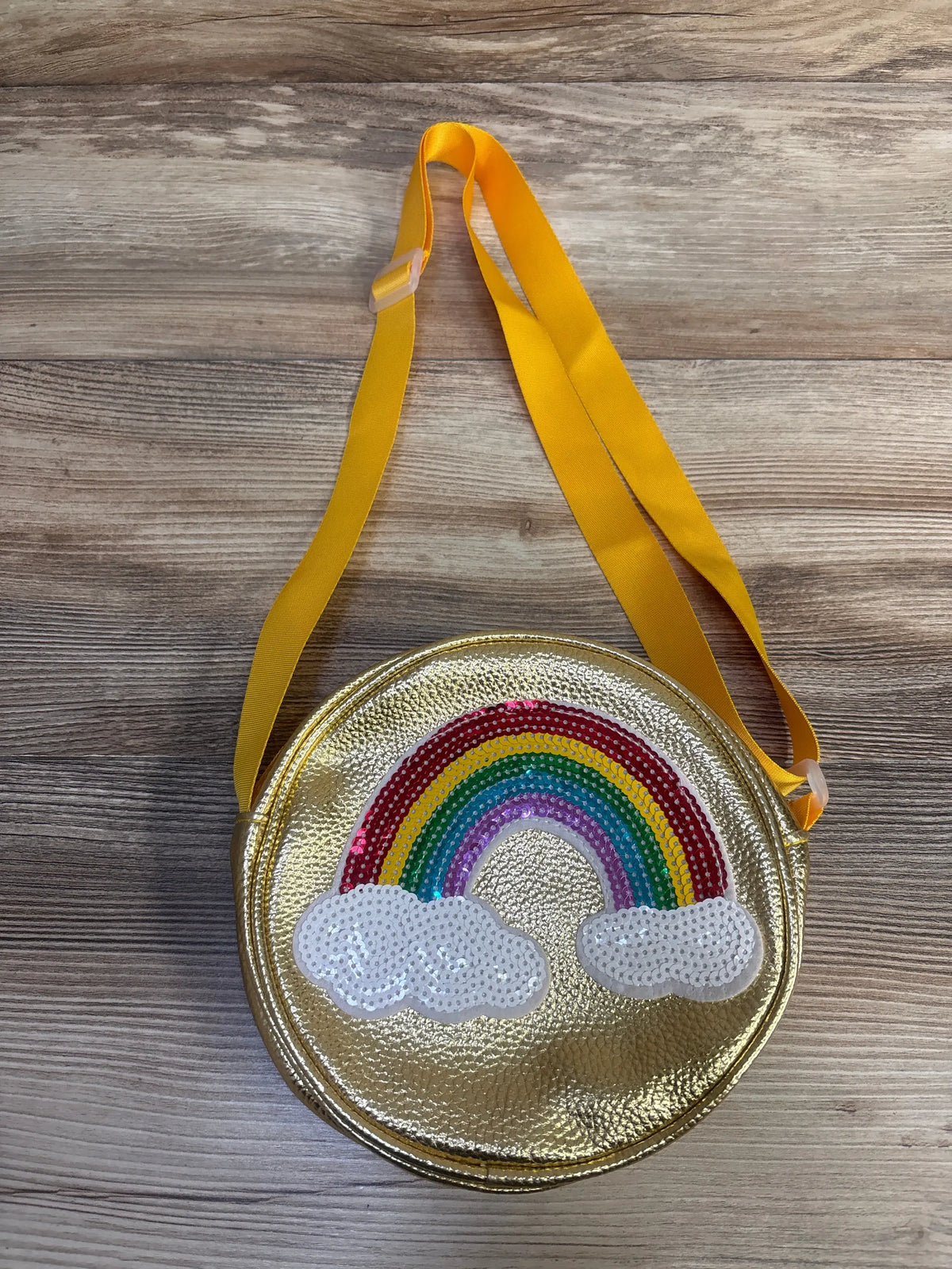 Front view of Sparkle Sisters gold sequin rainbow purse with cloud design and yellow shoulder strap on wood