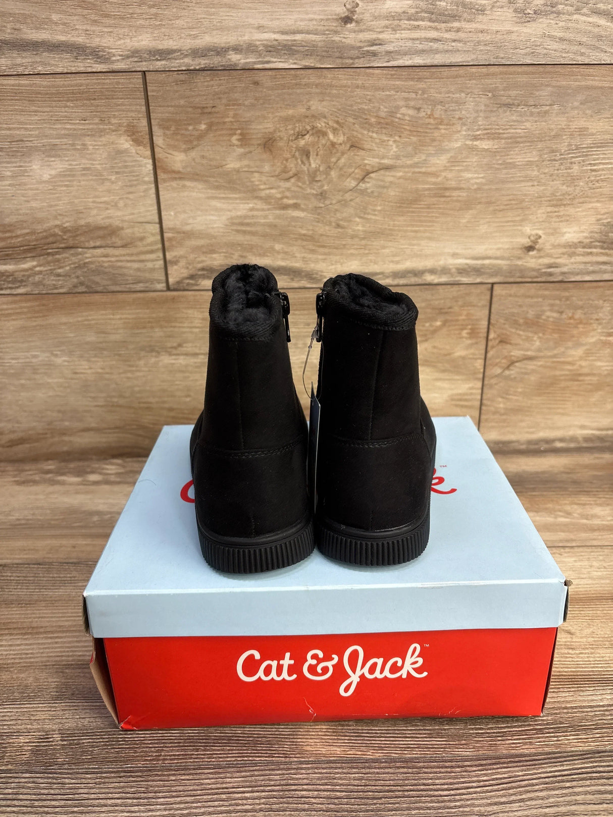 Pair of black Cat & Jack kids' winter boots with fur lining on a red and white Cat & Jack shoebox on wood background