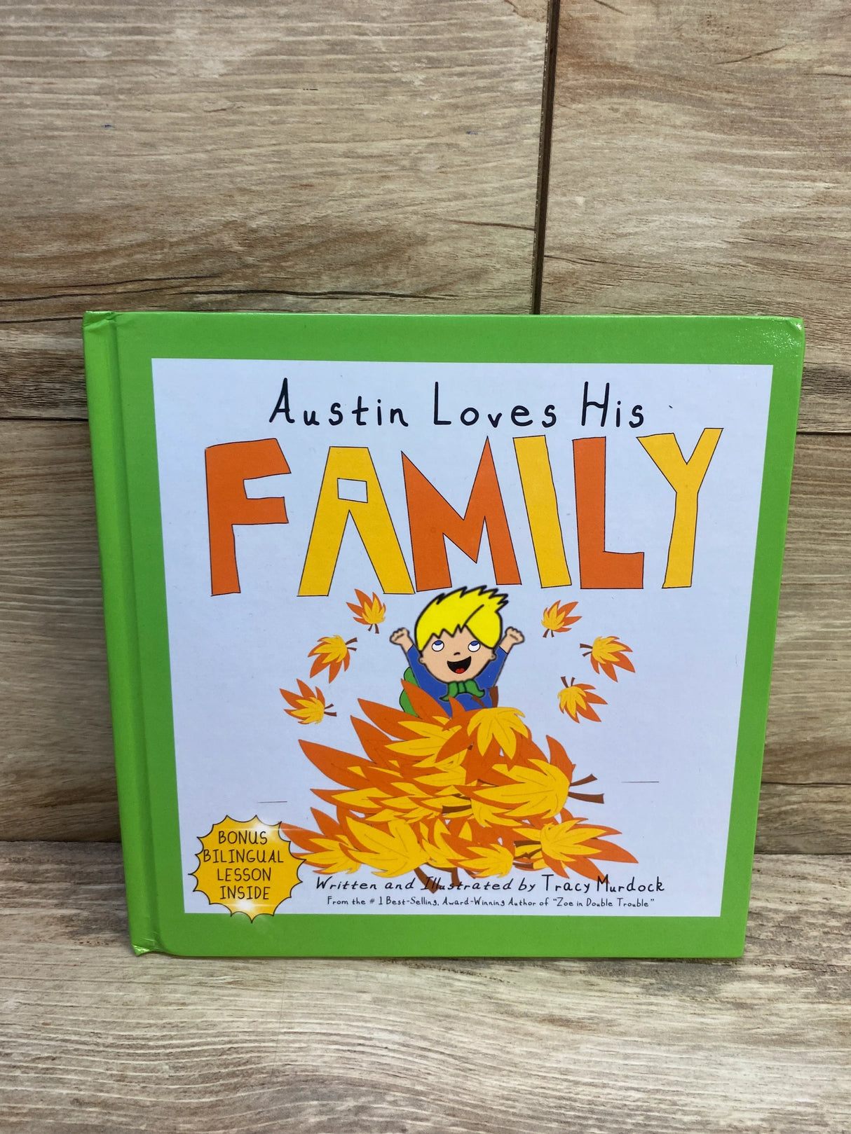 Front cover of Austin Loves His Family hardcover showing large FAMILY text and a child jumping into a pile of autumn leaves on wood