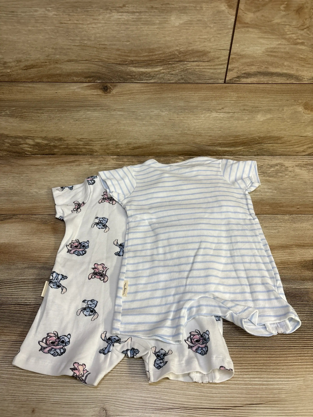 Front view of two white Sinsay Disney Lilo and Stitch shortie rompers, one character print and one pale blue striped, laid flat