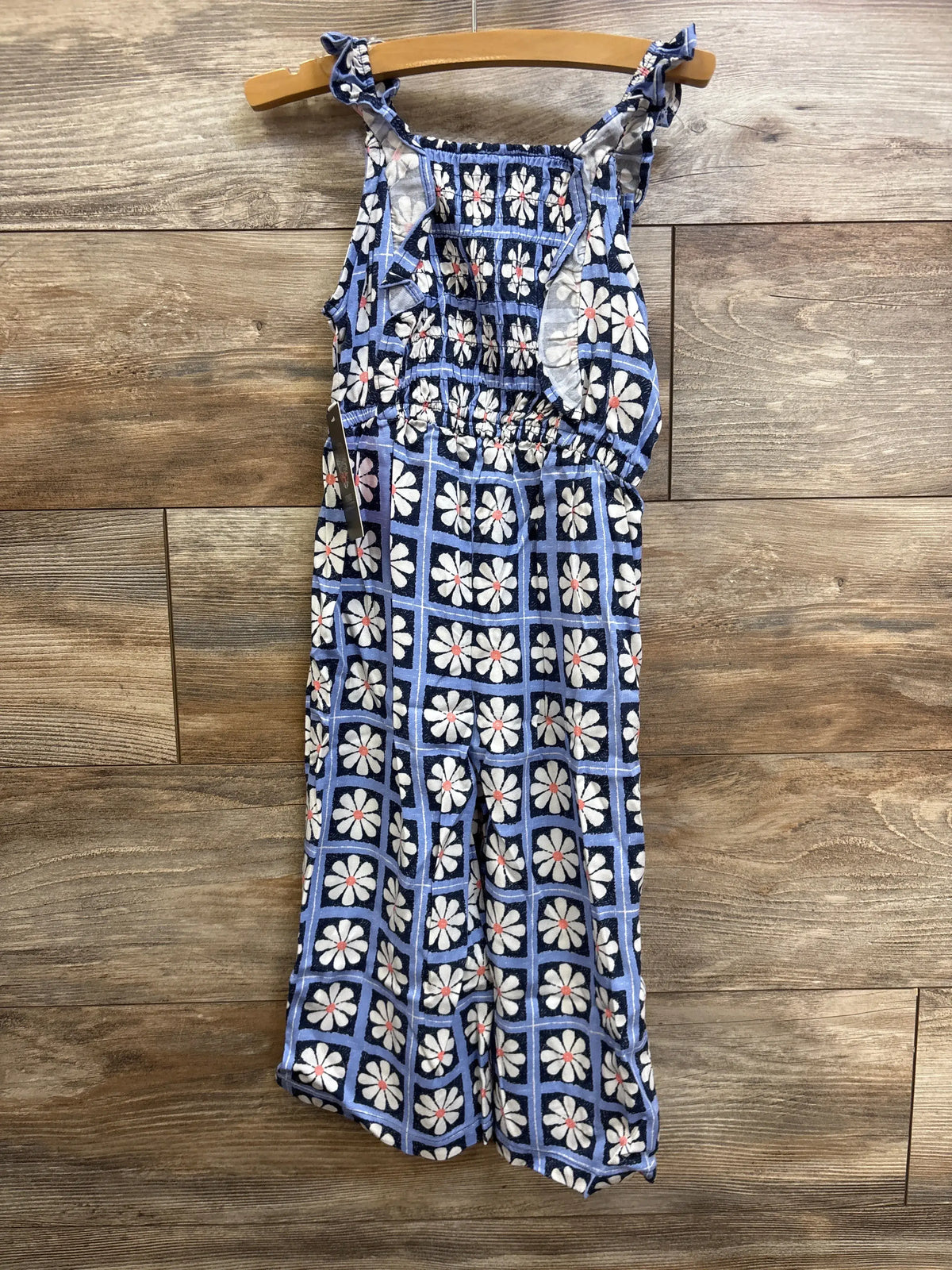 Front view of Vince Camuto blue floral smocked jumpsuit showcasing sleeveless design on a hanger against wood planks