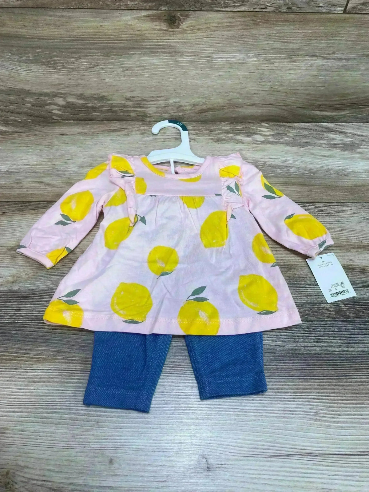 Flat-lay of baby long-sleeve pink lemon-print top with ruffle shoulders and matching blue leggings on wood floor