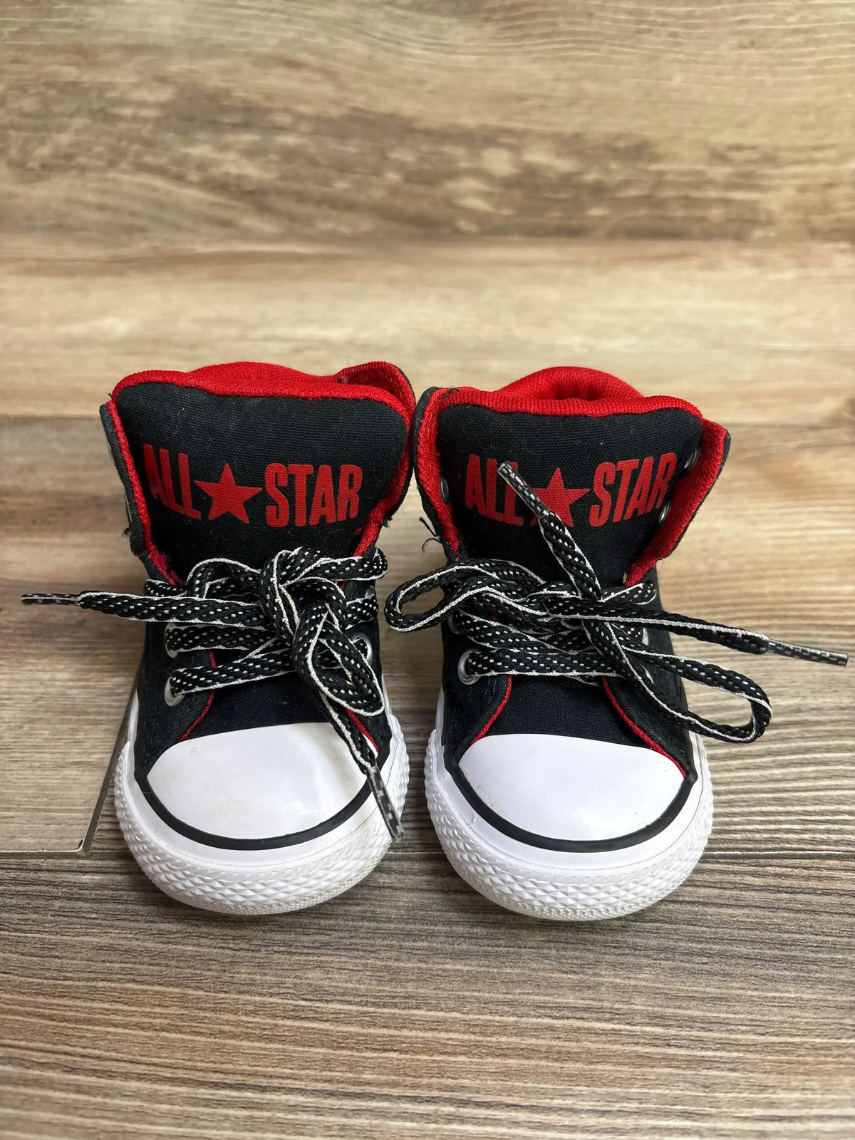Pair of black and red All Star sneakers with white rubber toe caps and black laces on wooden floor