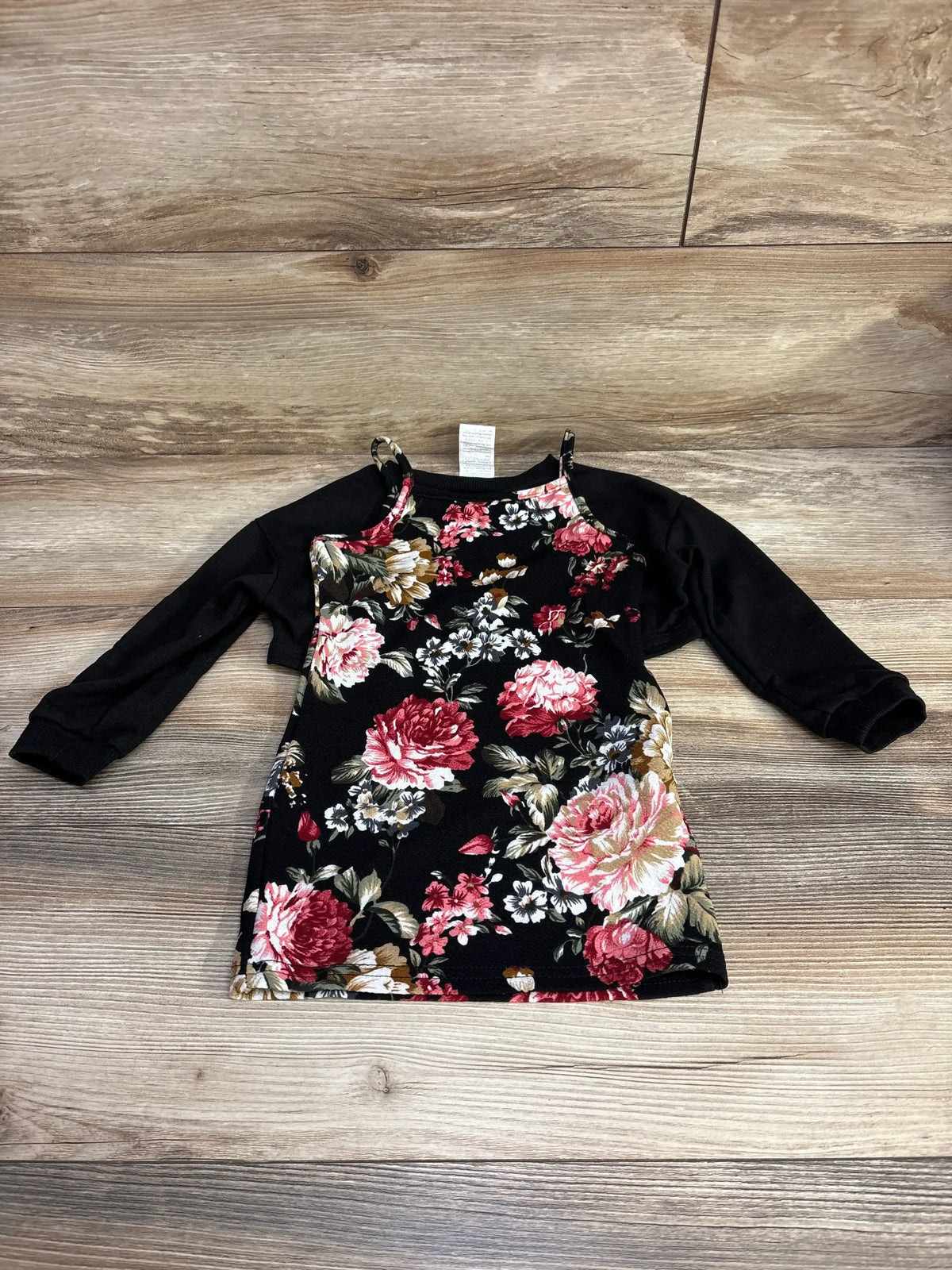 Flat lay of toddler 2-piece black floral dress set with a floral sleeveless dress layered over a black long-sleeve cropped top on wood