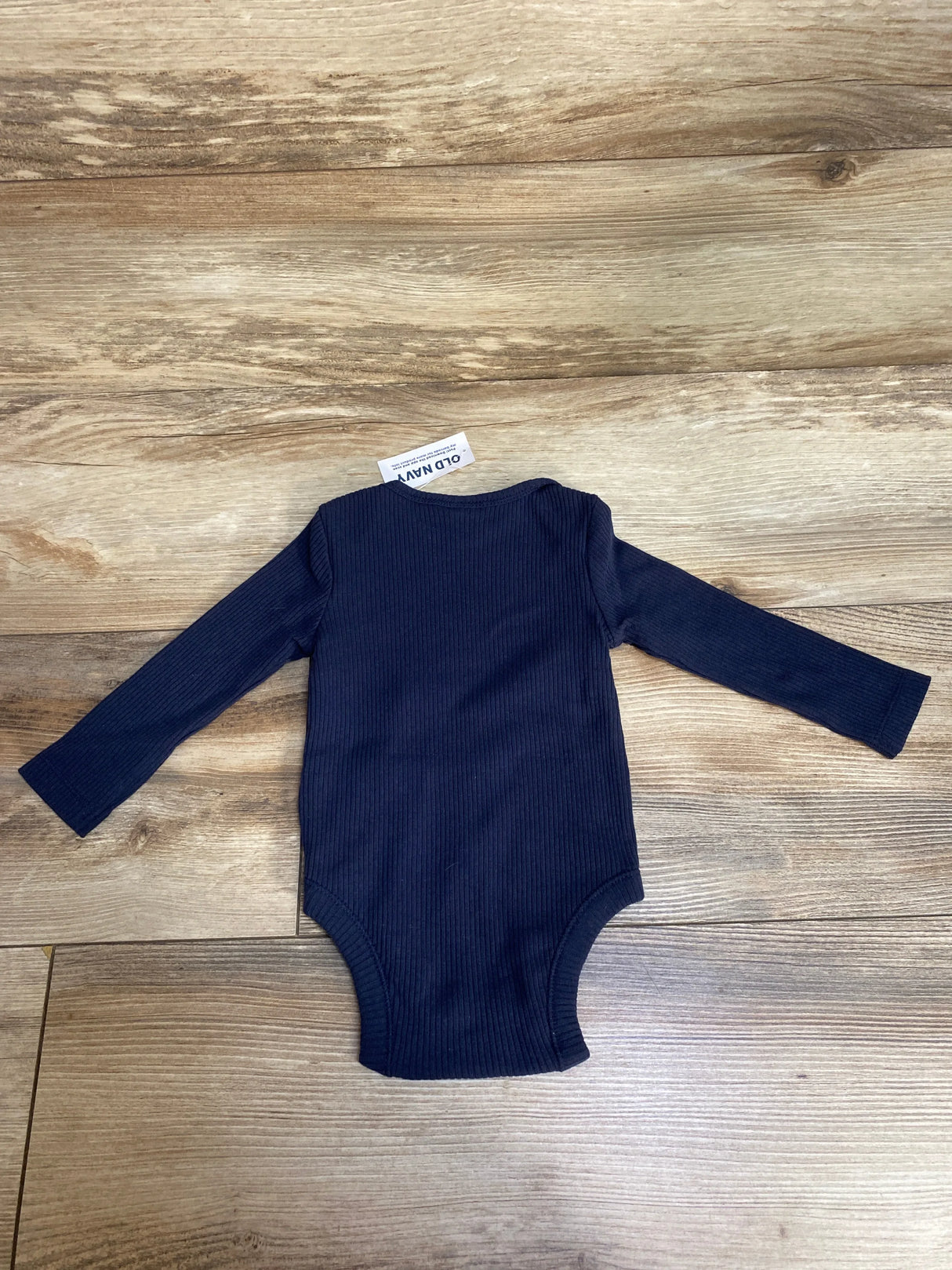Navy blue ribbed long-sleeve baby bodysuit laid flat on wooden floor with Old Navy tag