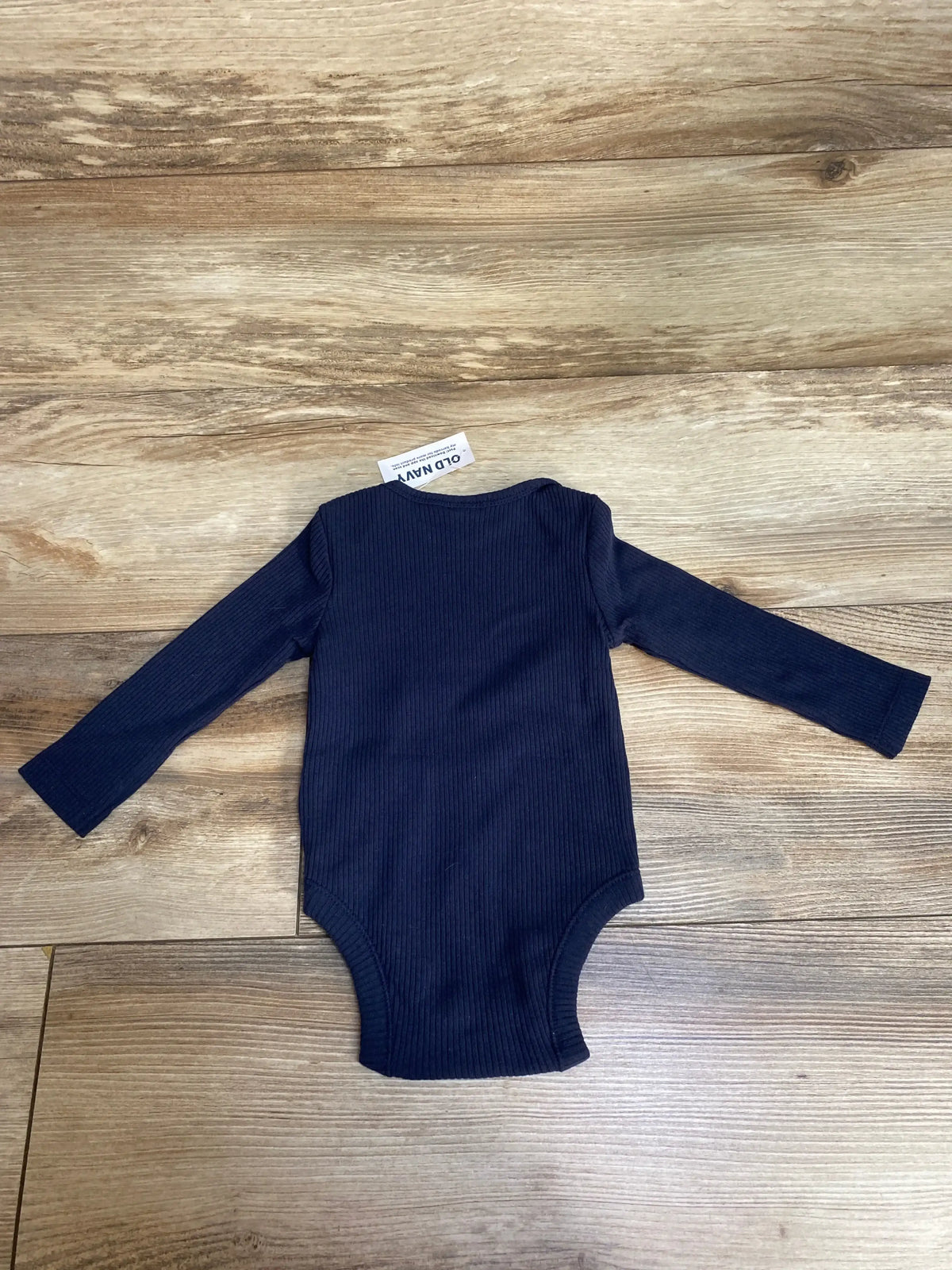 Navy blue ribbed long-sleeve baby bodysuit laid flat on wooden floor with Old Navy tag