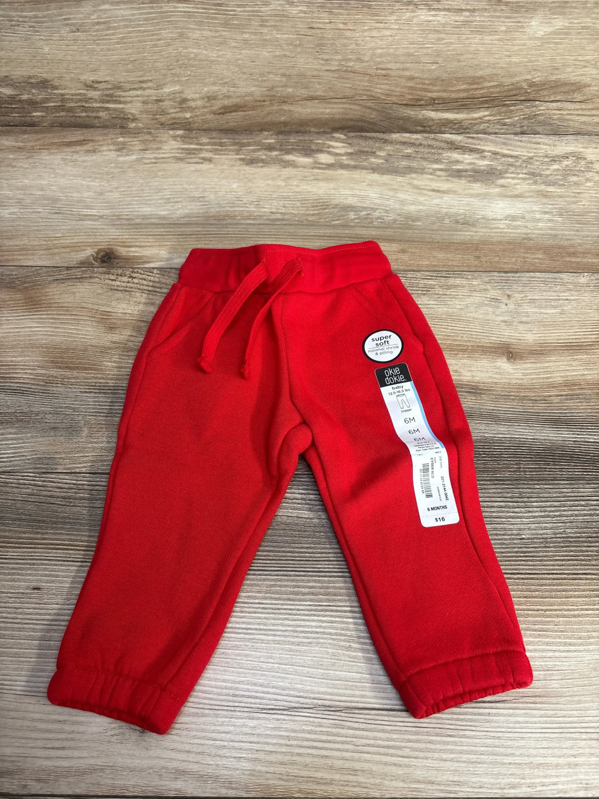 Red baby jogger pants size 6 months with drawstring and elastic cuffs on wooden surface